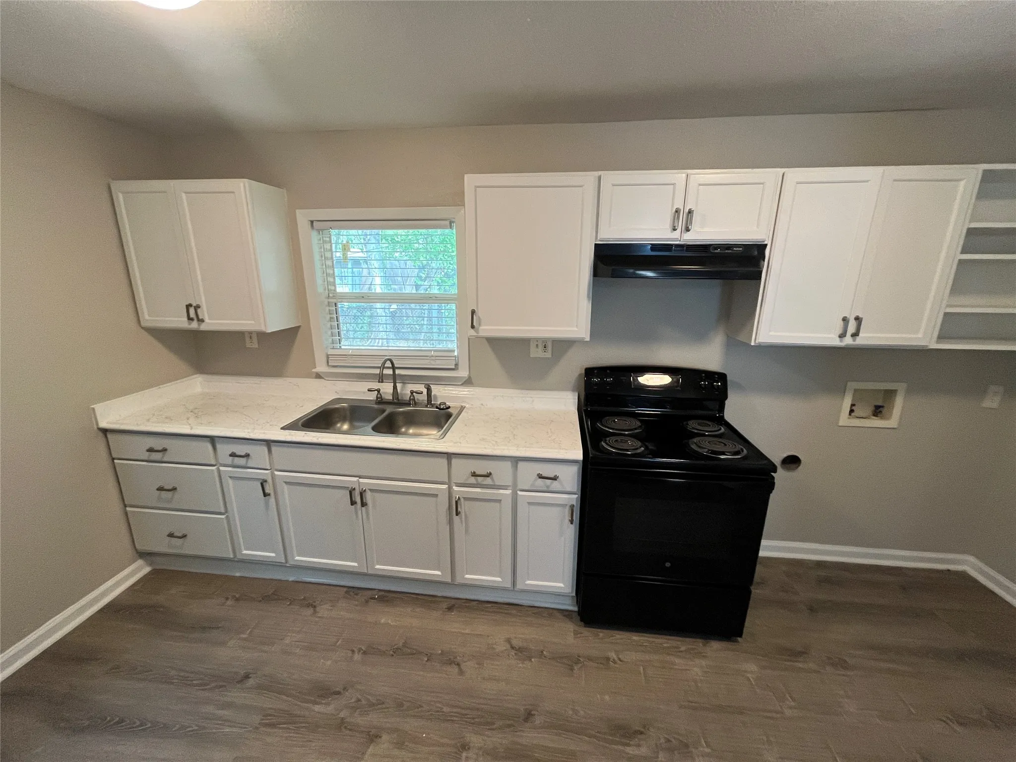 White cabinetry with matte black hardware, dual basin stainless steel sink, light-toned countertops, and wood-finish flooring