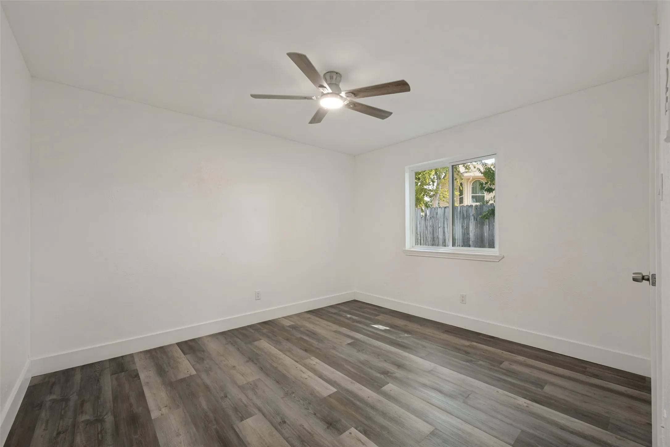 Wood-finish flooring, white walls, and a ceiling fan with integrated lighting