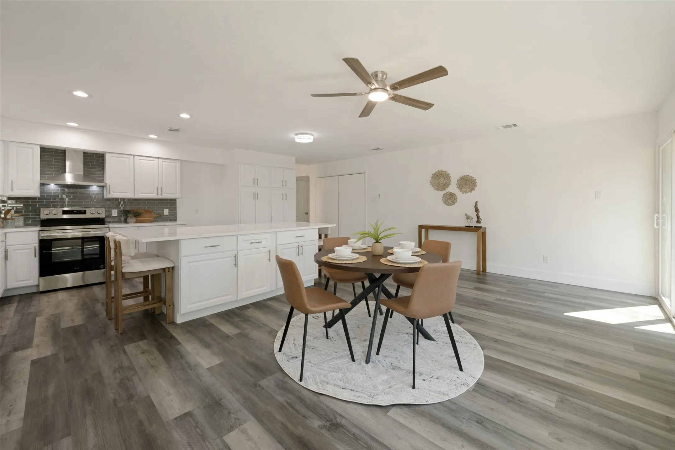 Open-concept kitchen and dining area featuring white cabinetry, a large kitchen island with white countertop, stainless steel appliances, and wood-finish flooring