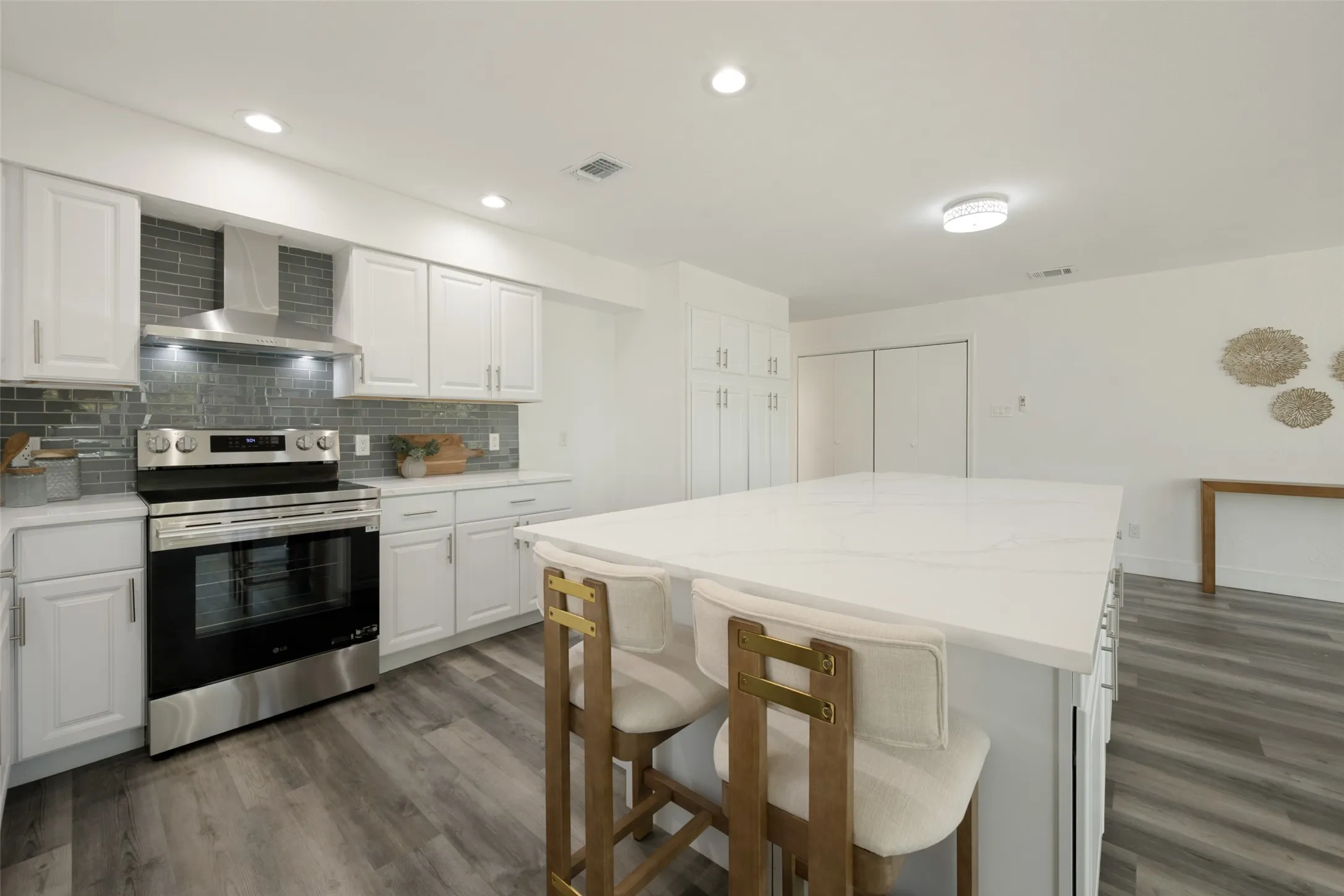 Kitchen featuring a large central island, white cabinetry, a tiled backsplash, and stainless steel appliances