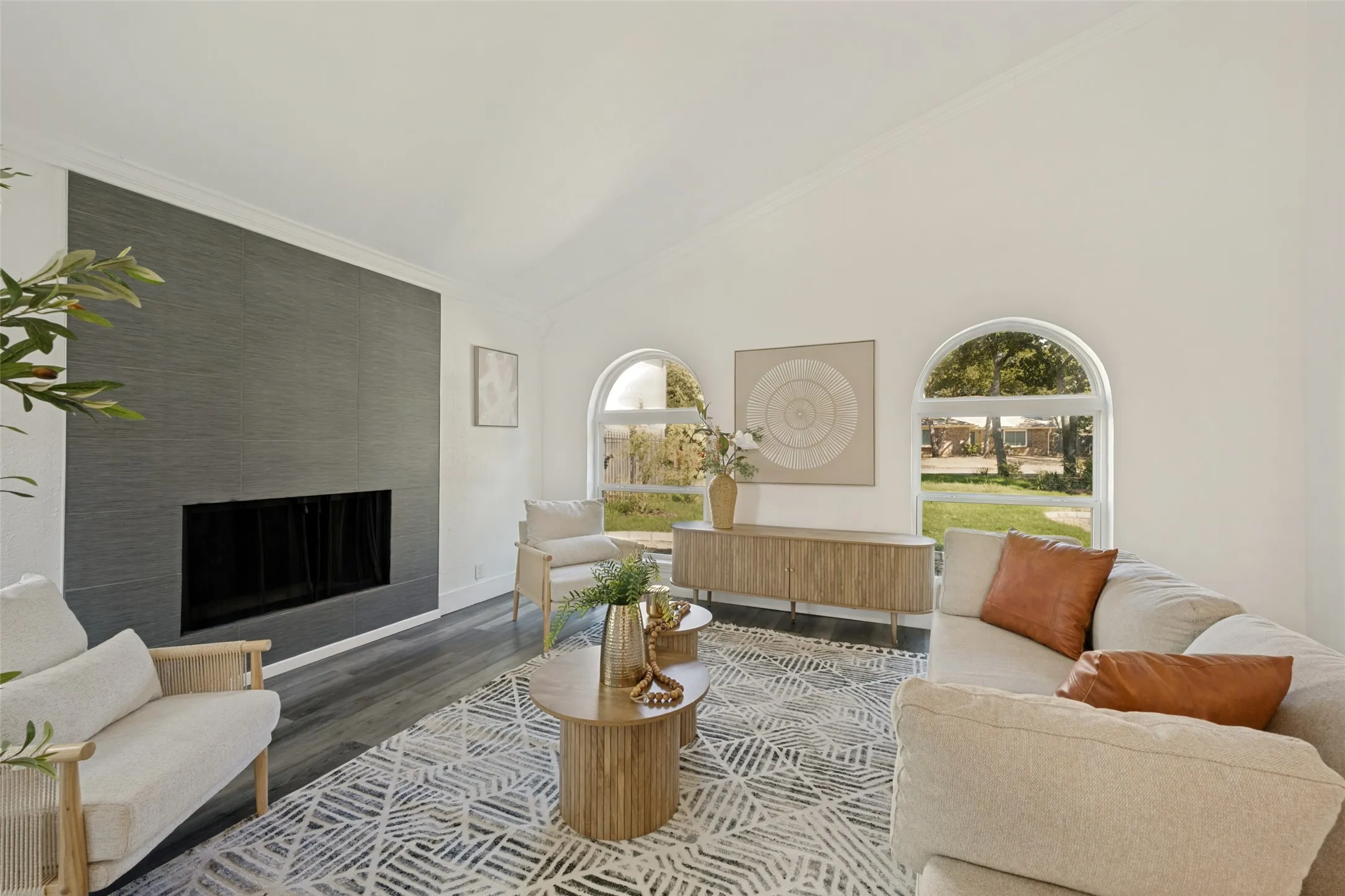 Vaulted ceilings, a full-height fireplace with a dark-toned surround, two arched windows, and wood-finish flooring