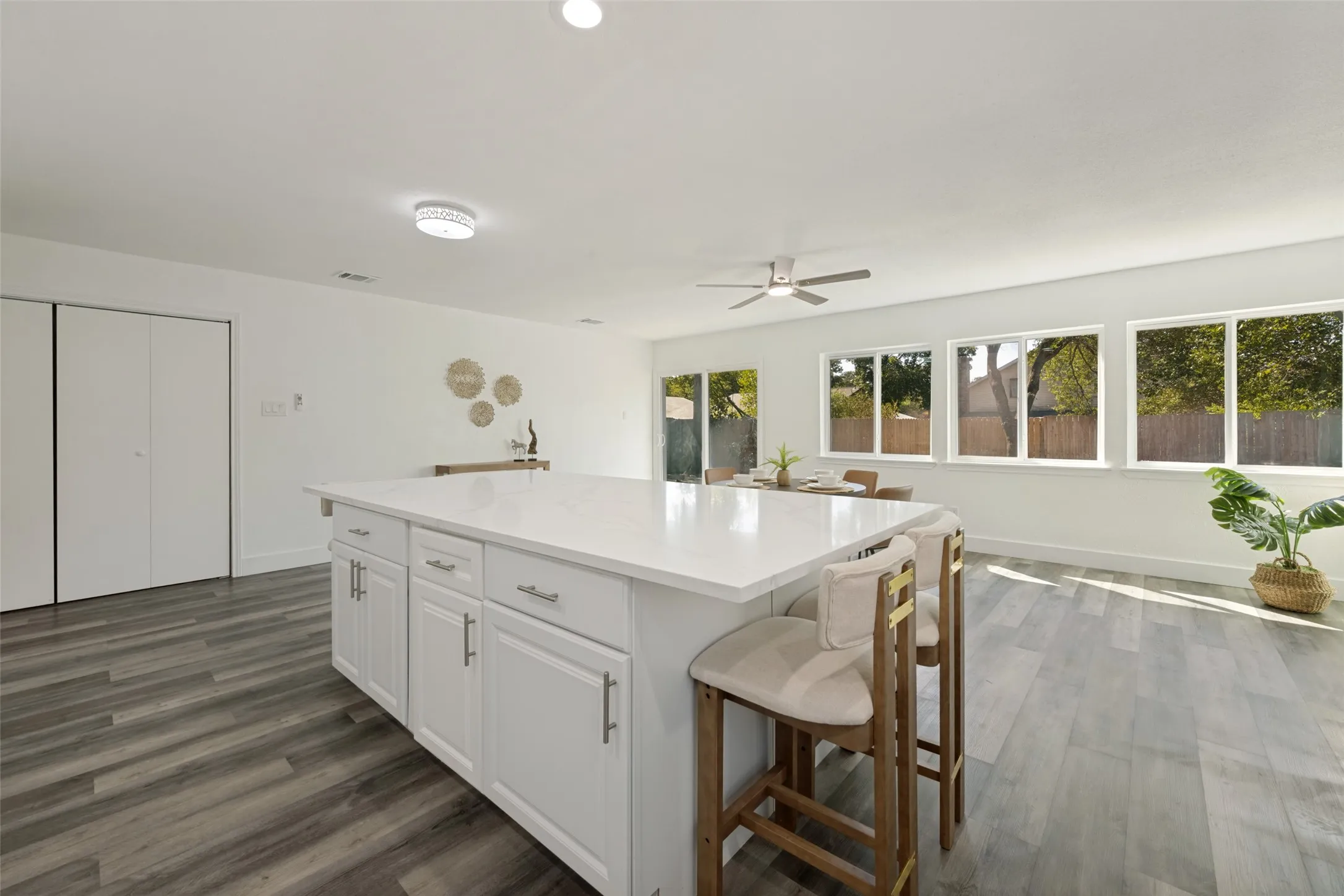 Spacious kitchen island with white cabinetry and a light-toned countertop, wood-finish flooring, recessed lighting, and multiple windows