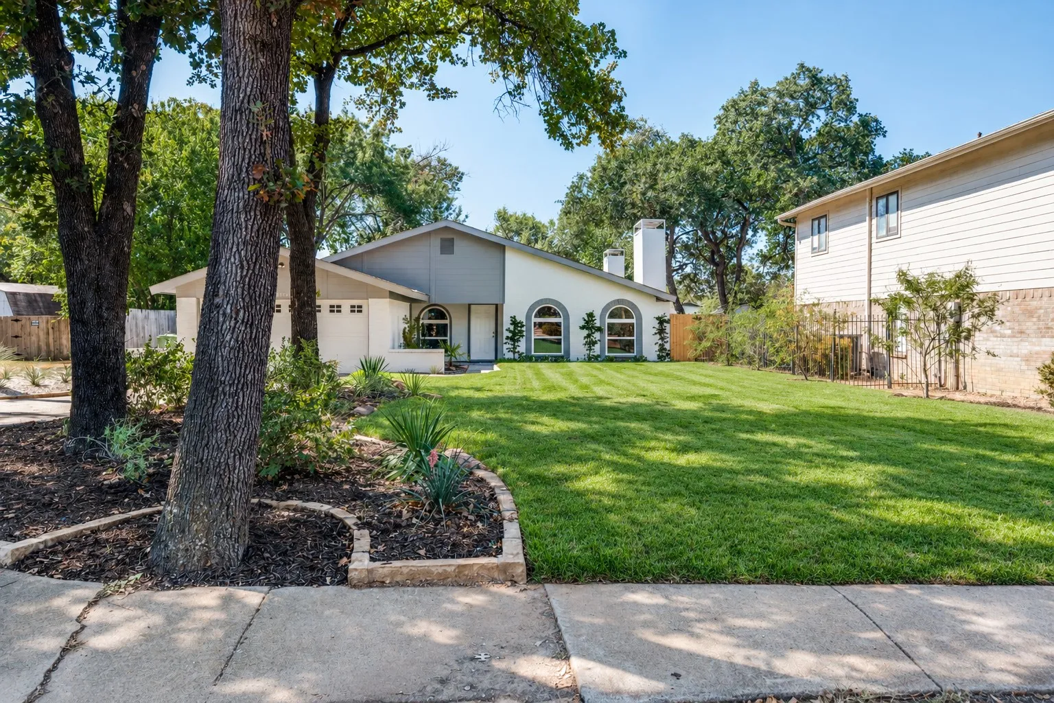 Ranch-style exterior with a stucco finish, multiple arched windows, a prominent chimney, and a well-maintained lawn