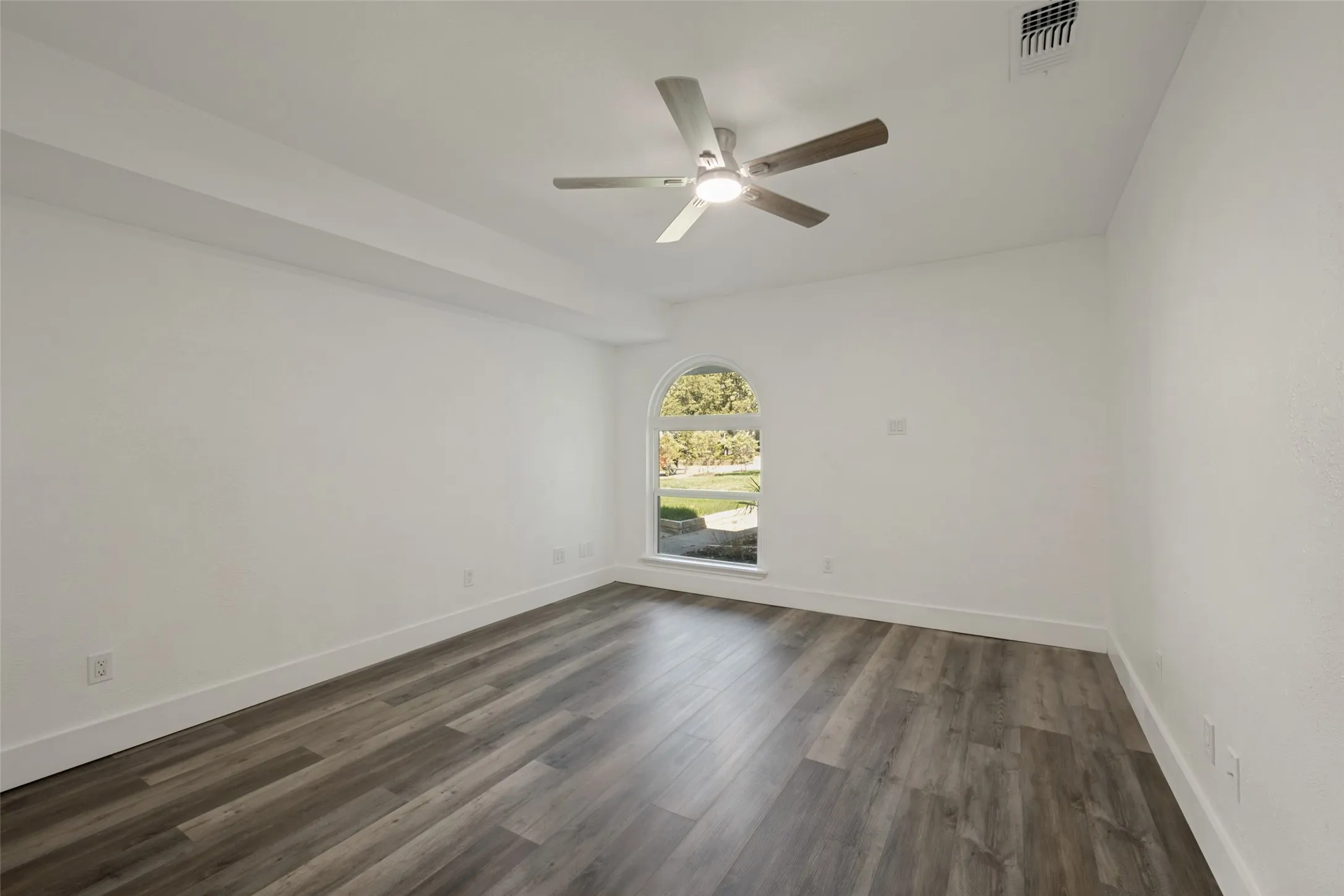 Arched window, wood-finish flooring, ceiling fan with integrated lighting, white walls, and white trim