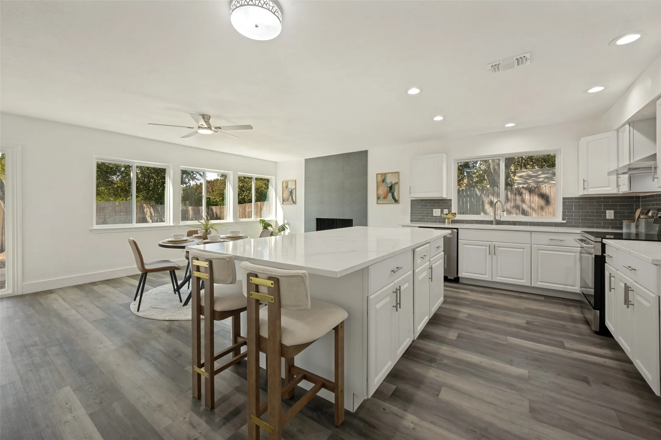 Spacious kitchen with a central island, white cabinetry, dark subway tile backsplash, and wood-finish flooring