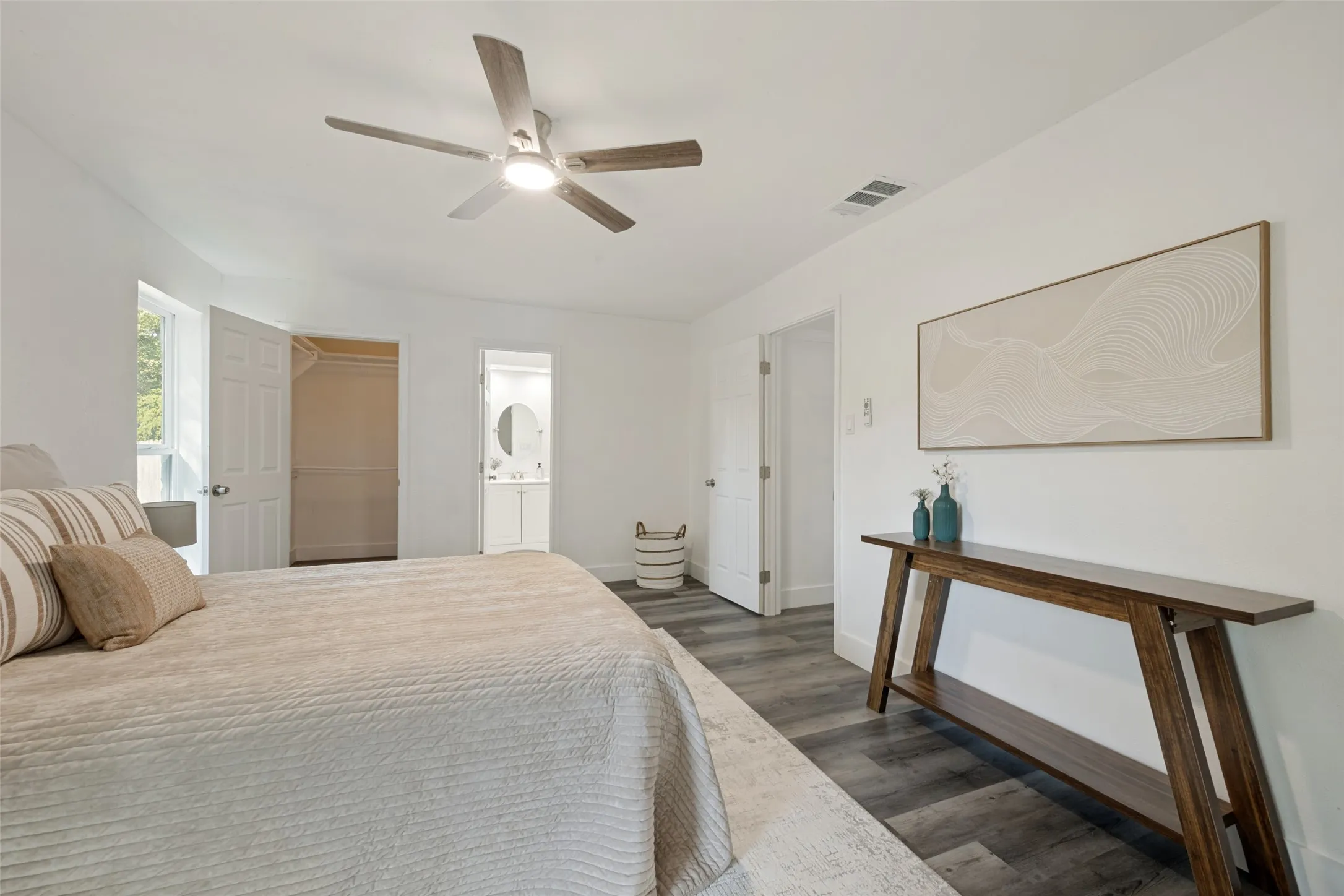 Wood-finish flooring, ceiling fan with integrated lighting, built-in closet with shelving, and an en-suite bathroom with a circular mirror and vanity