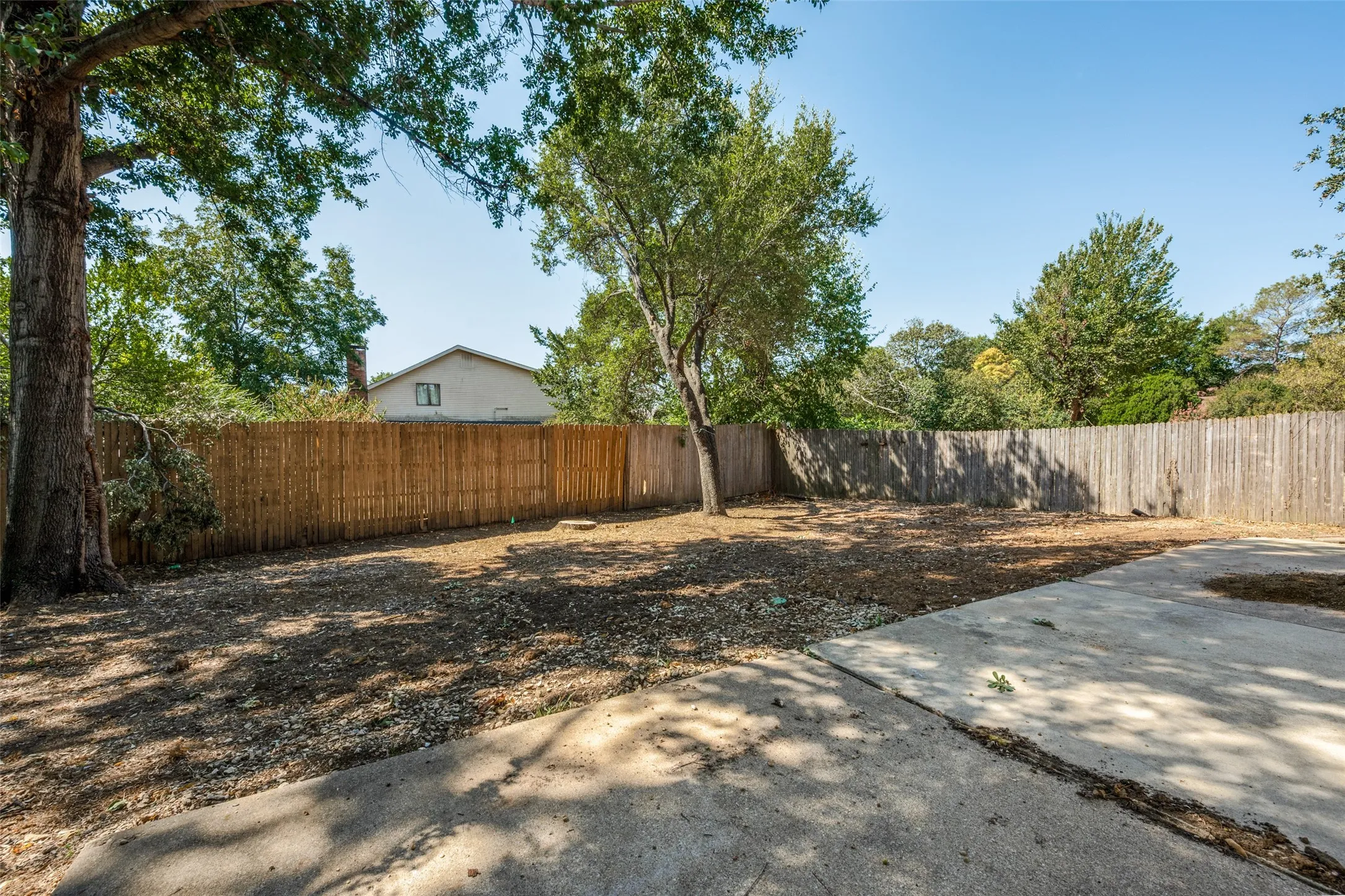 Spacious rear yard with mature trees and a concrete patio
