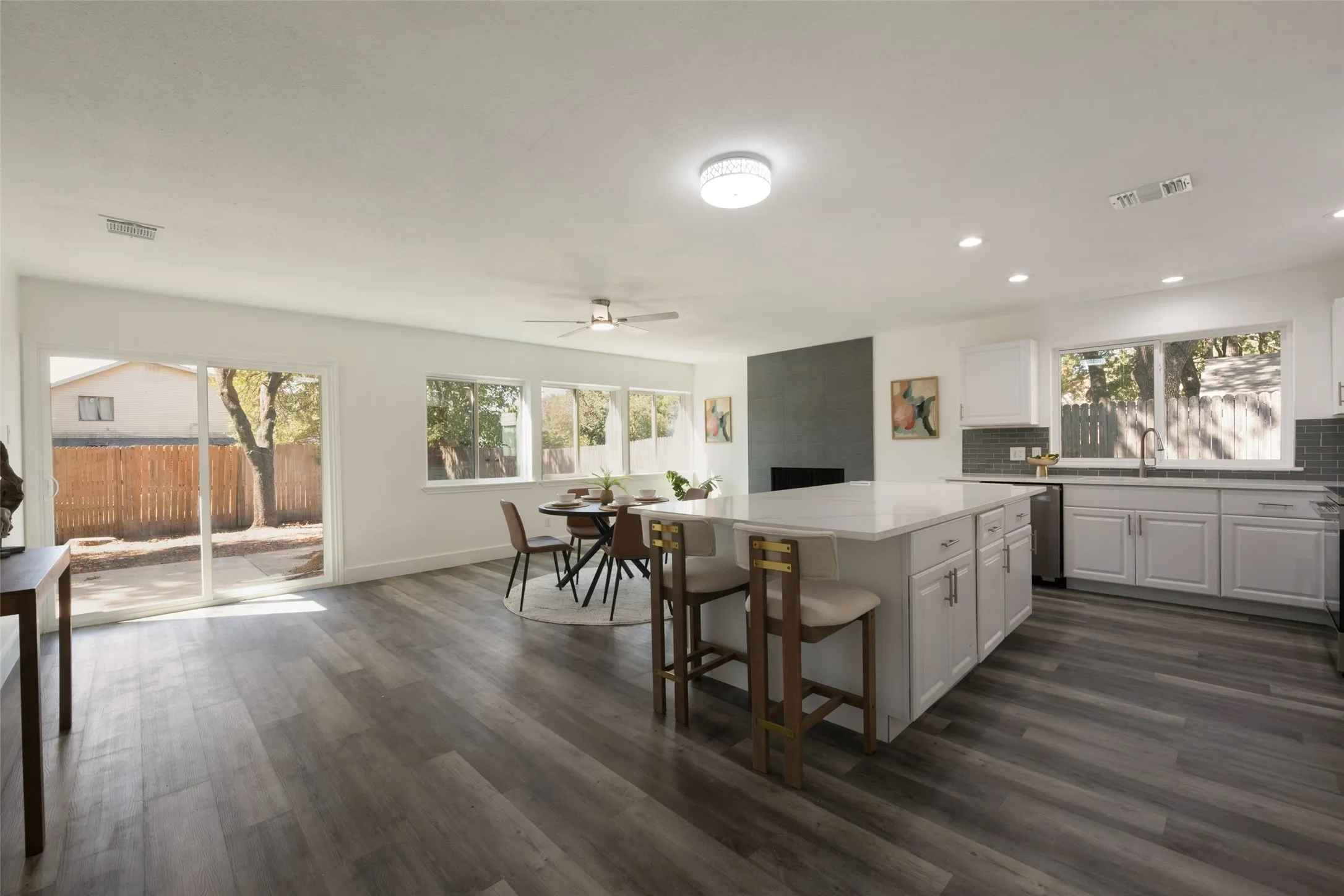 Contemporary kitchen featuring an island with a light-toned countertop, white cabinetry with silver-toned hardware, and a gray tile backsplash