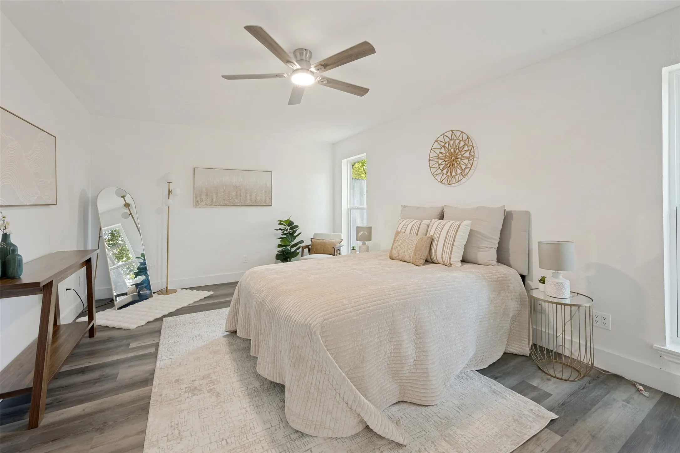 White walls, wood-finish flooring, ceiling fan with integrated lighting, and multiple windows