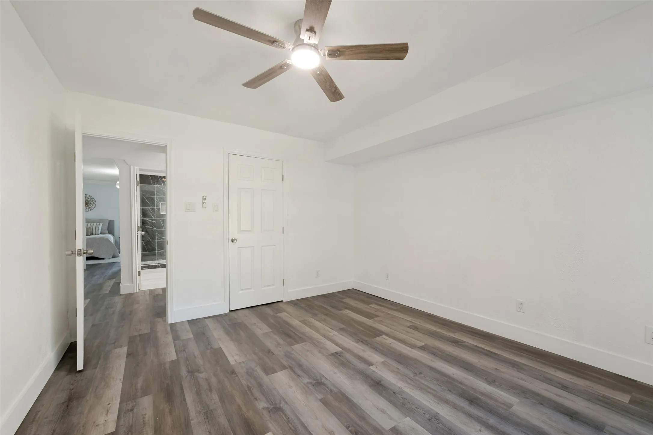 Wood-finish flooring, white walls, white trim, ceiling fan with light, and white paneled doors