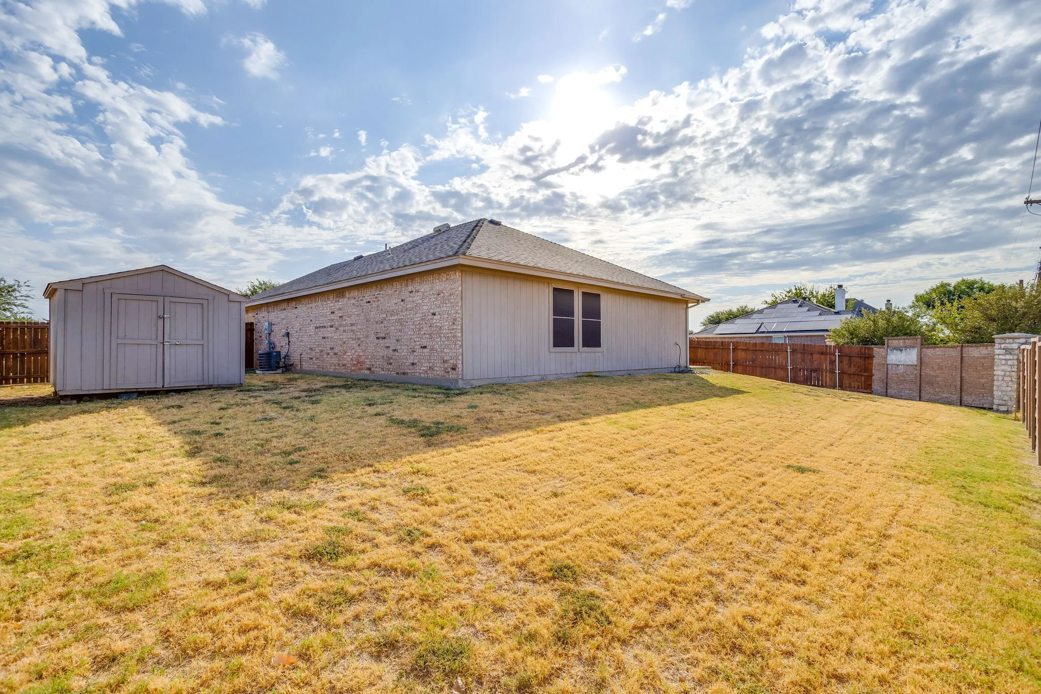 Spacious backyard featuring a storage shed, brick and siding exterior, and wood fencing