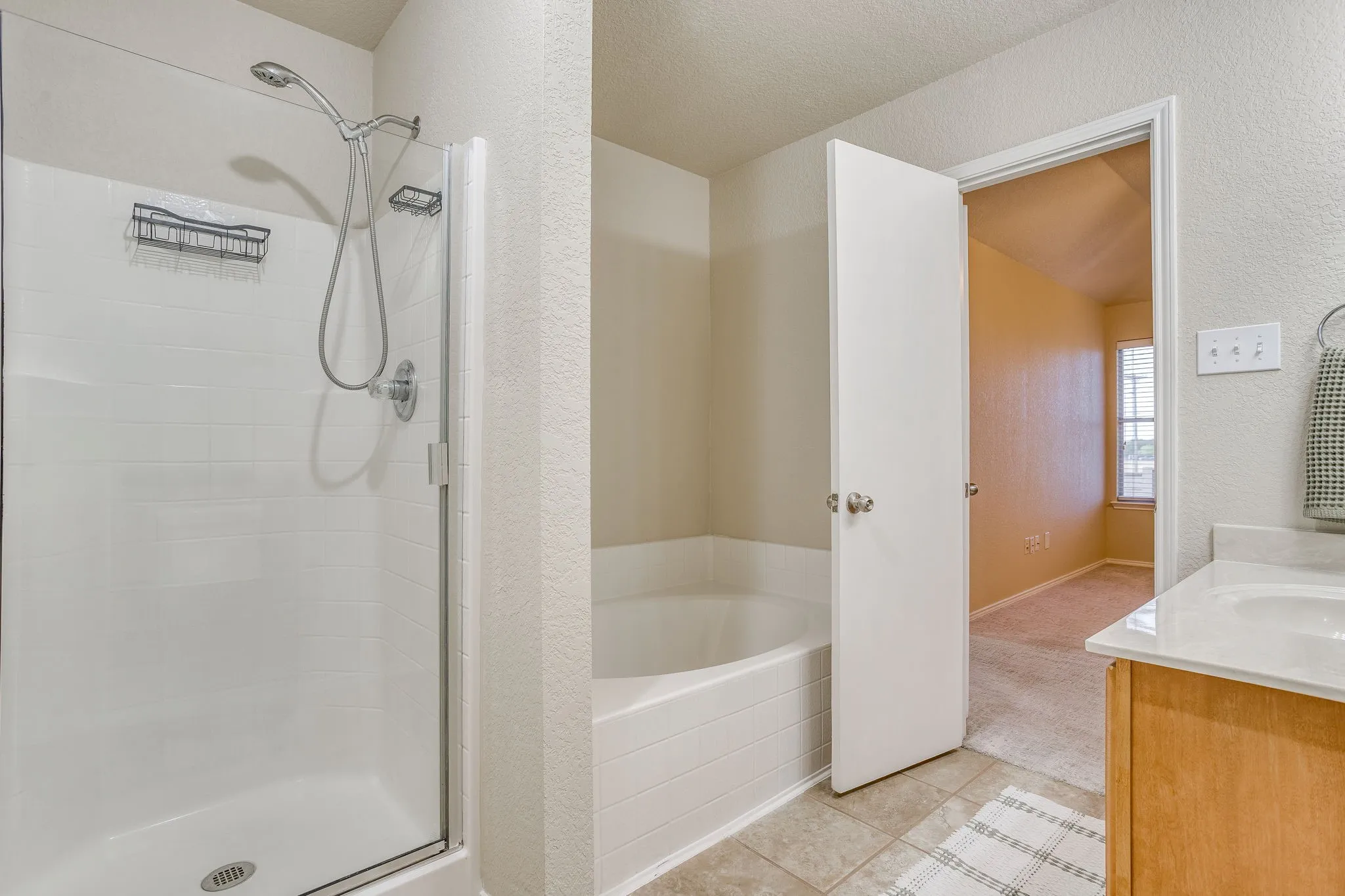 Shower with glass enclosure, separate soaking tub, wood-finish vanity, and integrated sink