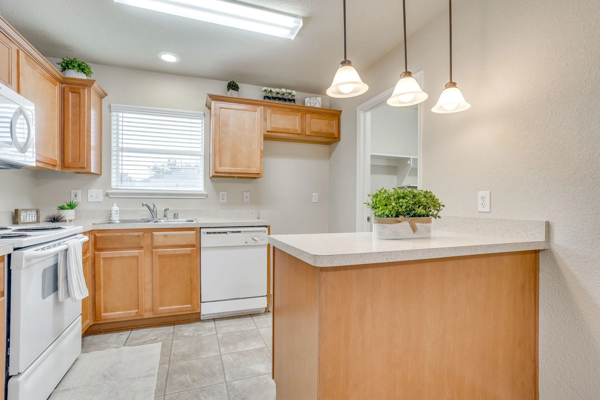 Kitchen featuring light wood cabinetry, light-toned countertops, tile flooring, and a window with blinds