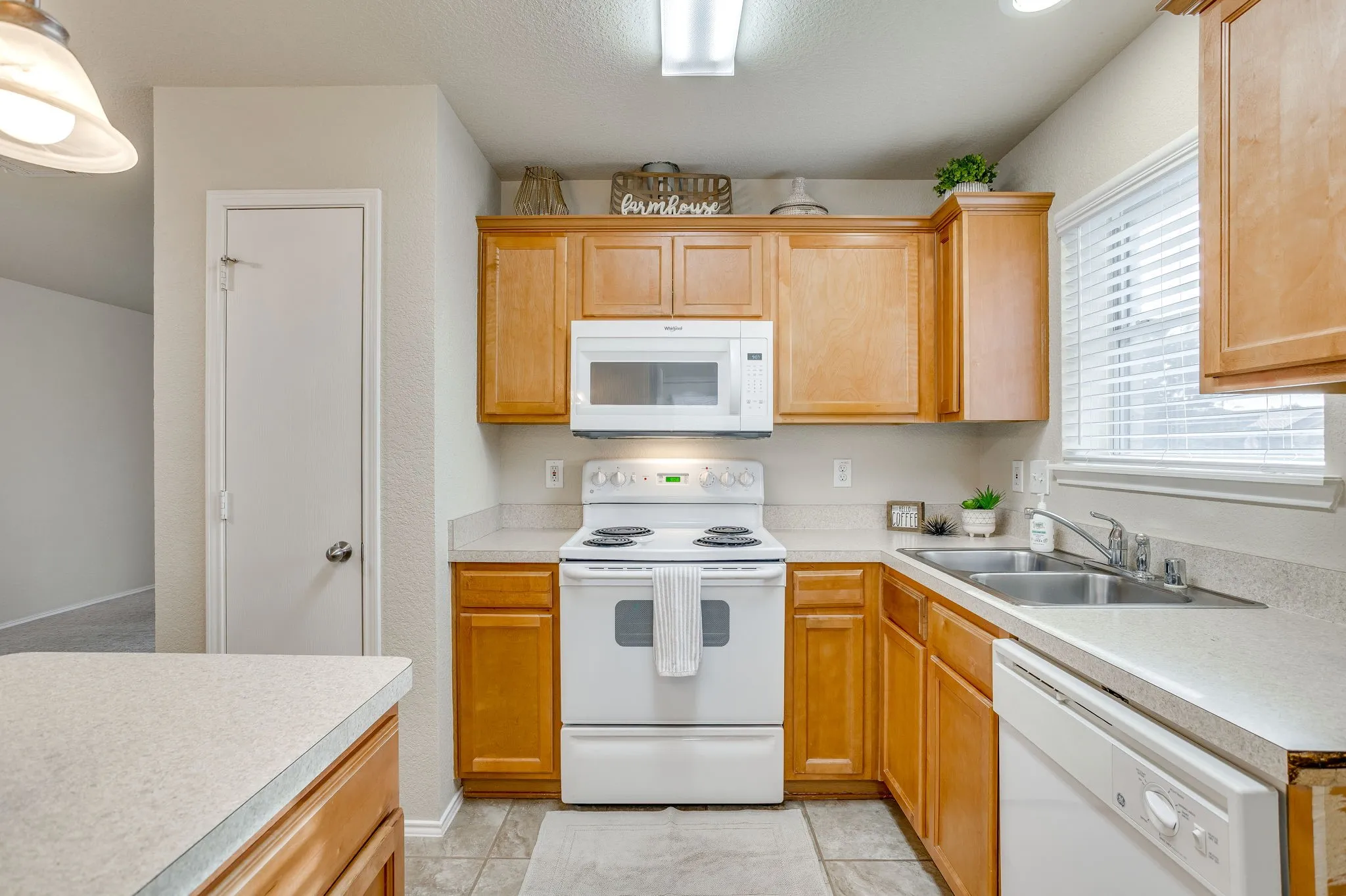 Kitchen with wood-finish cabinetry, light-colored countertops, white appliances, and a double basin sink