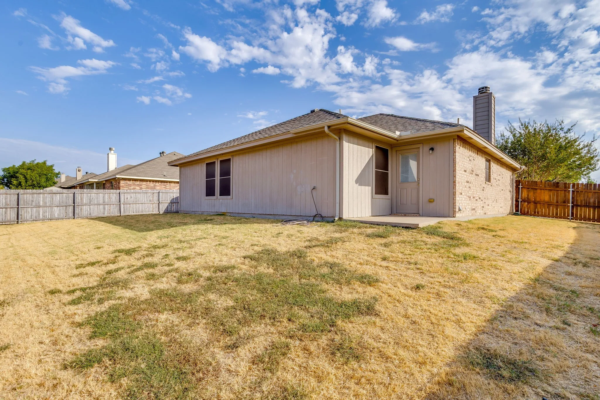 Expansive backyard featuring a wood privacy fence, concrete patio, and brick exterior accents