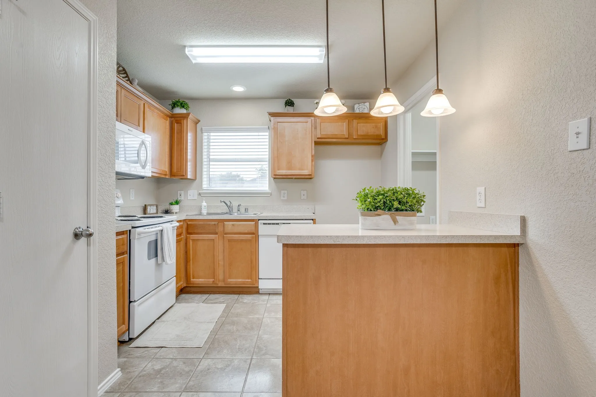 Kitchen featuring wood cabinetry, white appliances, tile flooring, a window with blinds, and pendant lighting