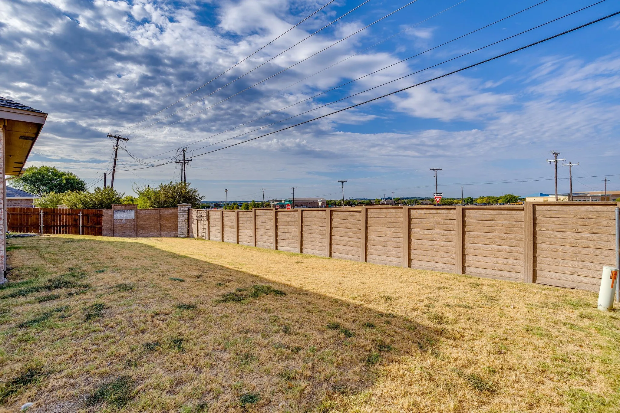 Backyard featuring extensive fencing, a combination of wood and concrete panel fencing, and a side exterior wall with brick finish