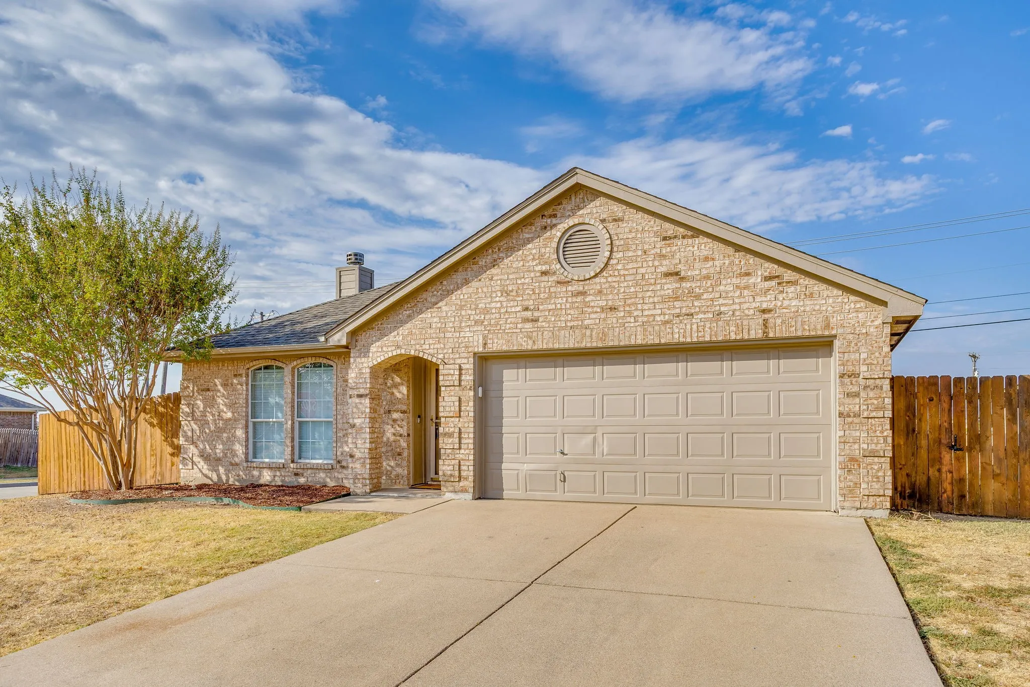 Brick exterior with a gabled roofline, attached garage, concrete driveway, and privacy fencing