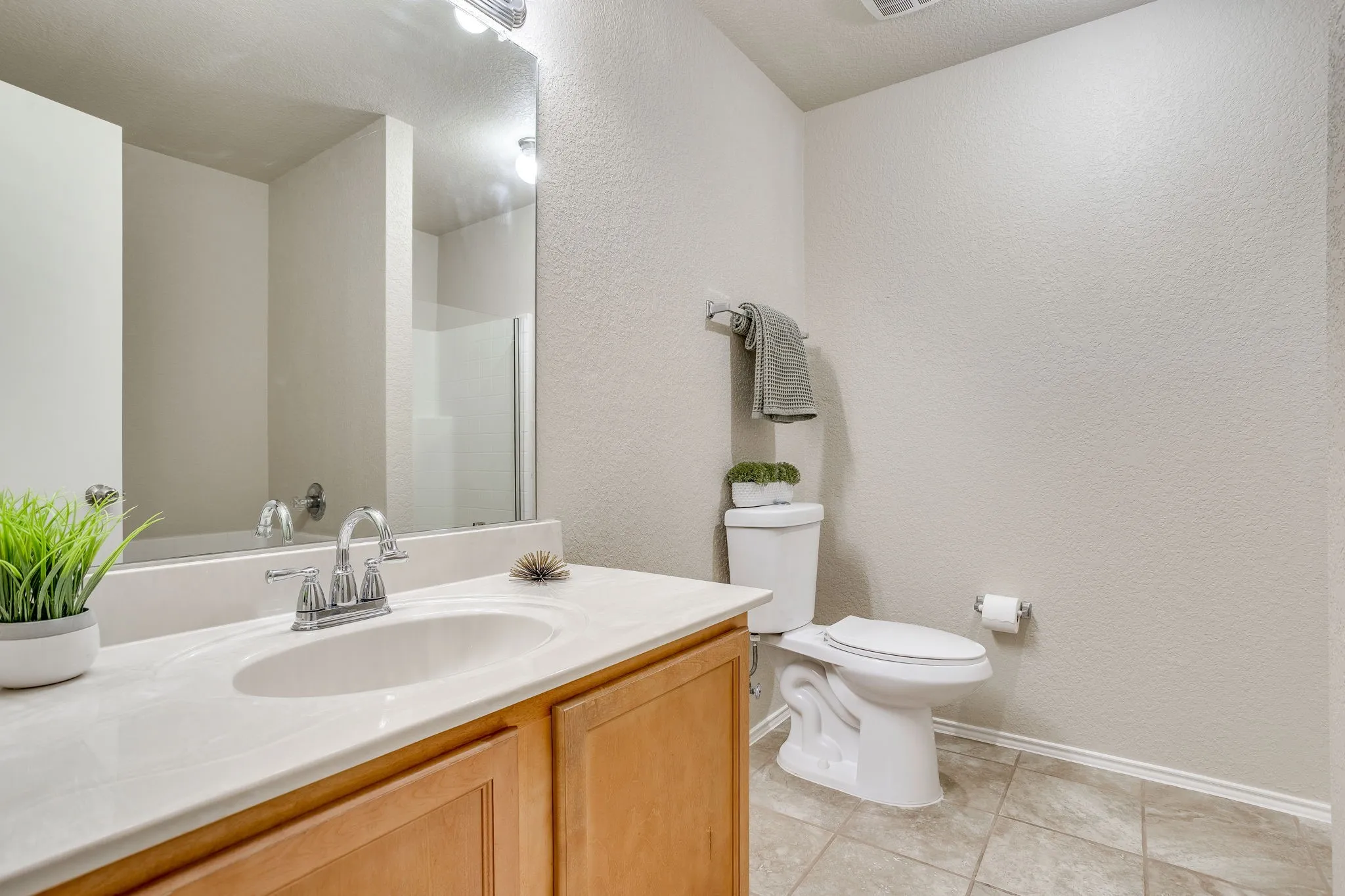 Wood-finish vanity with an integrated sink and chrome faucet, large wall mirror, and neutral-toned floor tile