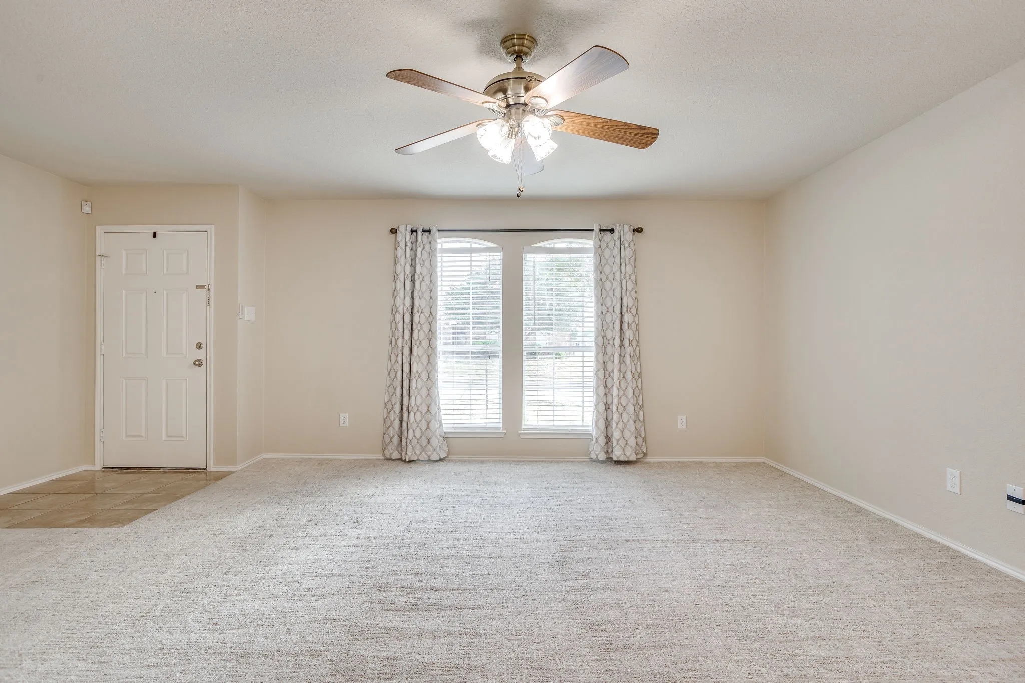 Carpeted living area with a ceiling fan, arched window, and tile flooring entry