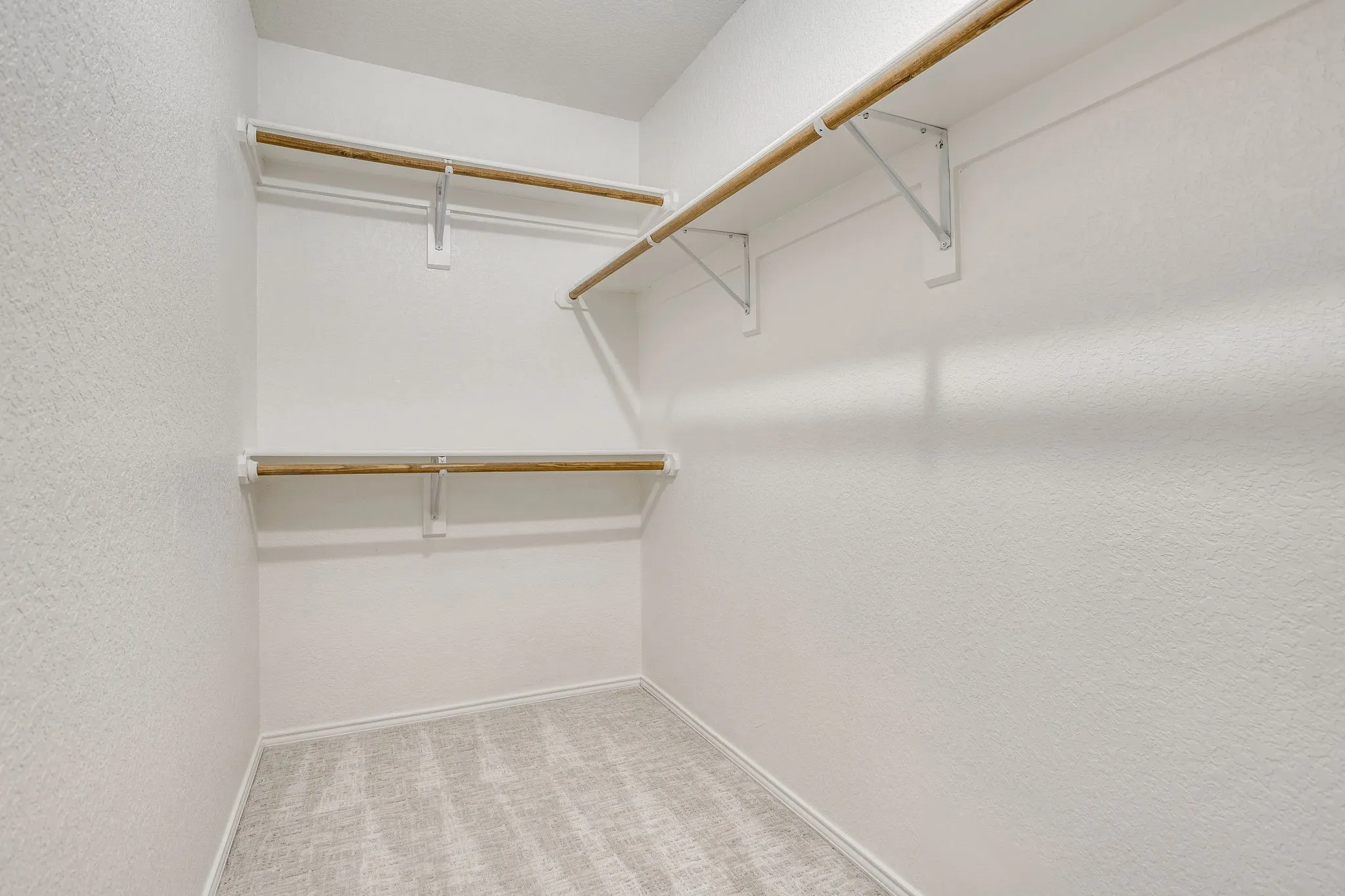 Walk-in closet featuring light-colored carpeting and multiple storage rods