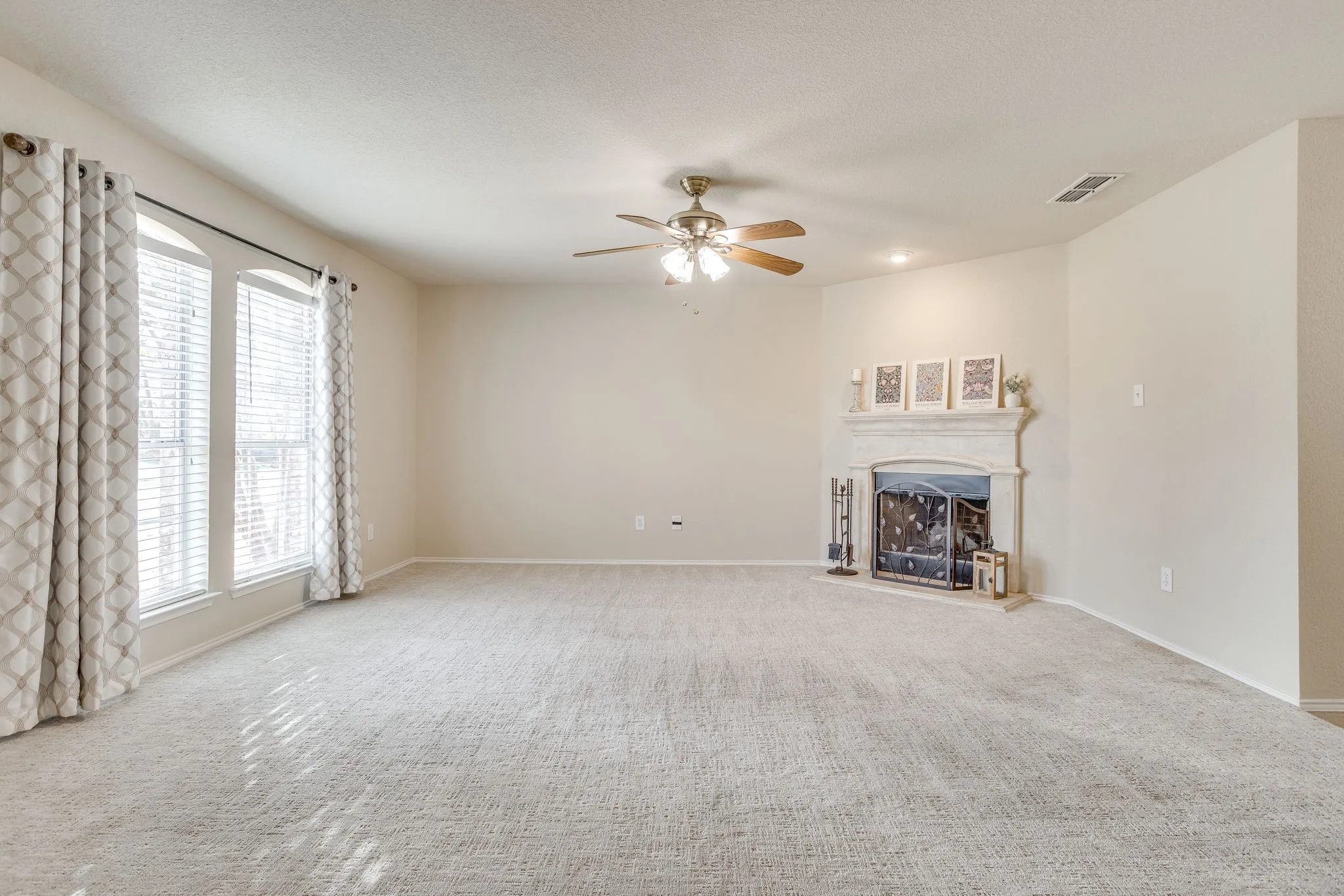 Expansive carpeted room featuring a ceiling fan, arched windows with blinds, and a fireplace with a mantel