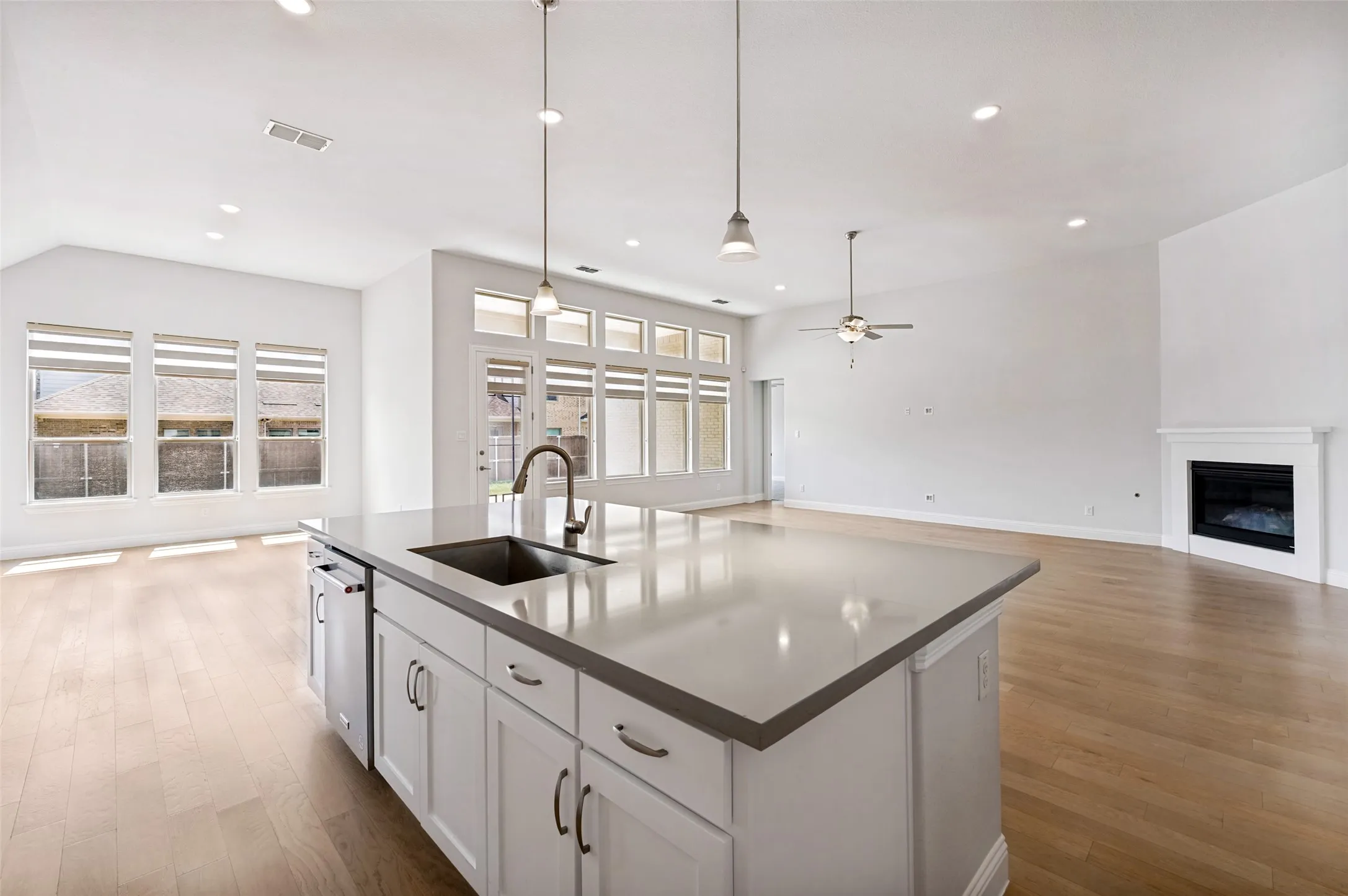 Expansive open-concept living, dining, and kitchen areas create a bright and impressive space designed for effortless everyday living and entertaining. Soaring ceilings, beautiful hardwood floors, and walls of windows fill the home with natural light, while the oversized kitchen island anchors the space. The seamless flow into the spacious living room, complete with a cozy fireplace, creates a warm and inviting heart of the home.