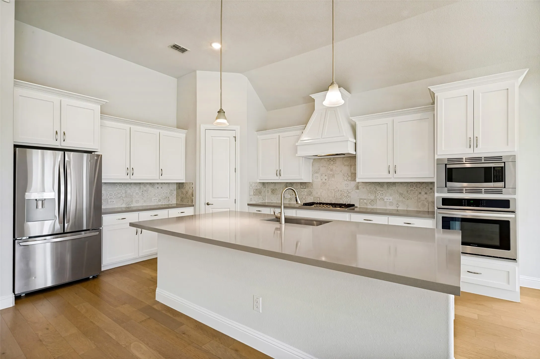 This spacious, light-filled kitchen is designed for both everyday living and entertaining, featuring abundant white cabinetry, quartz countertops, stainless steel appliances, and a beautiful decorative tile backsplash.