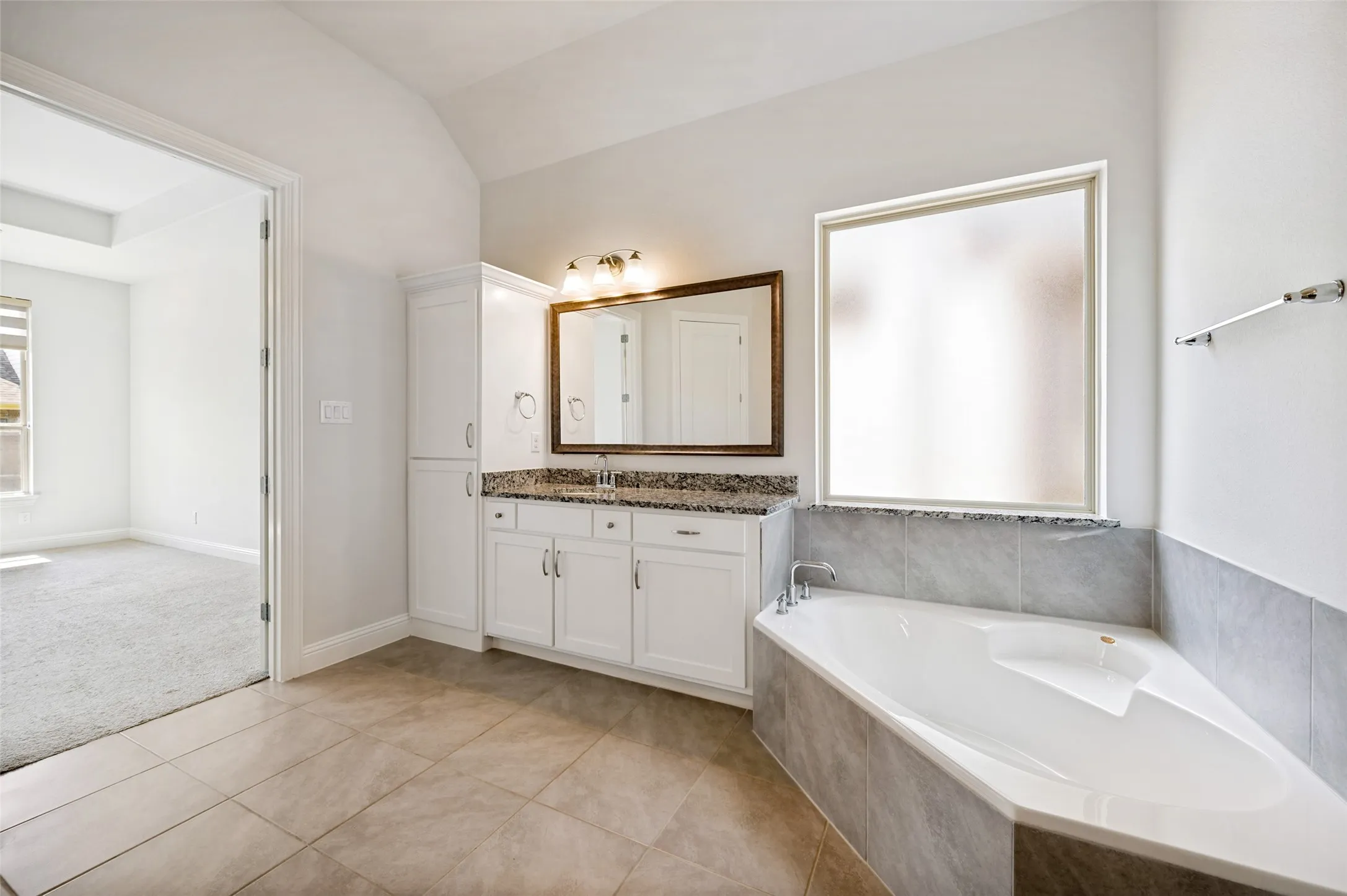 Spacious primary ensuite bath featuring a relaxing garden tub, generous vanity with granite countertops, abundant cabinetry, and additional built-in storage. Neutral tile and a large frosted window create a bright, serene space designed for both comfort and functionality.