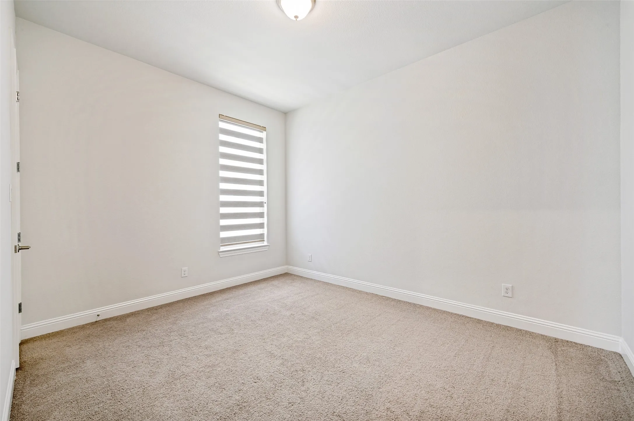 Spacious secondary bedroom featuring soft neutral carpeting, a large window with decorative shade, and plenty of natural light. The generous layout offers ample space for comfortable furnishings, while a walk-in closet provides excellent storage, making this an inviting and functional retreat for family or guests.