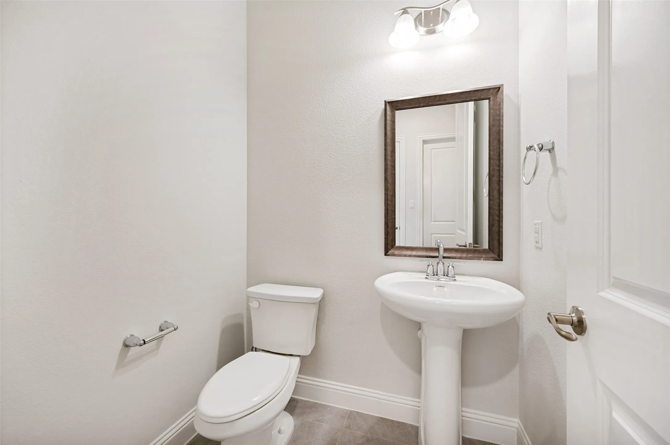 Conveniently located half bath is perfect for guests, featuring a classic pedestal sink, framed mirror, neutral finishes, and a clean, timeless design.