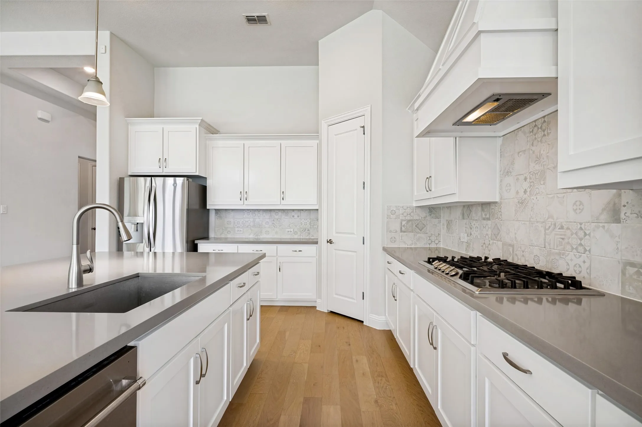Beautifully designed kitchen featuring crisp white cabinetry, the oversized island offers abundant prep space and seating, while a gas-burning cooktop with statement vent hood, generous cabinetry, and spacious walk-in pantry provide exceptional functionality and storage.