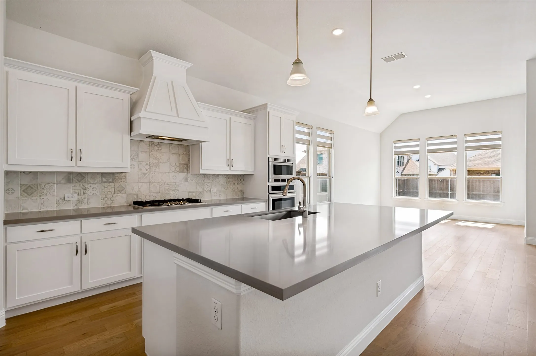 The oversized island provides exceptional prep space and generous seating, while the gas cooktop, statement vent hood, built-in oven and microwave, and soaring ceilings add both style and functionality.
