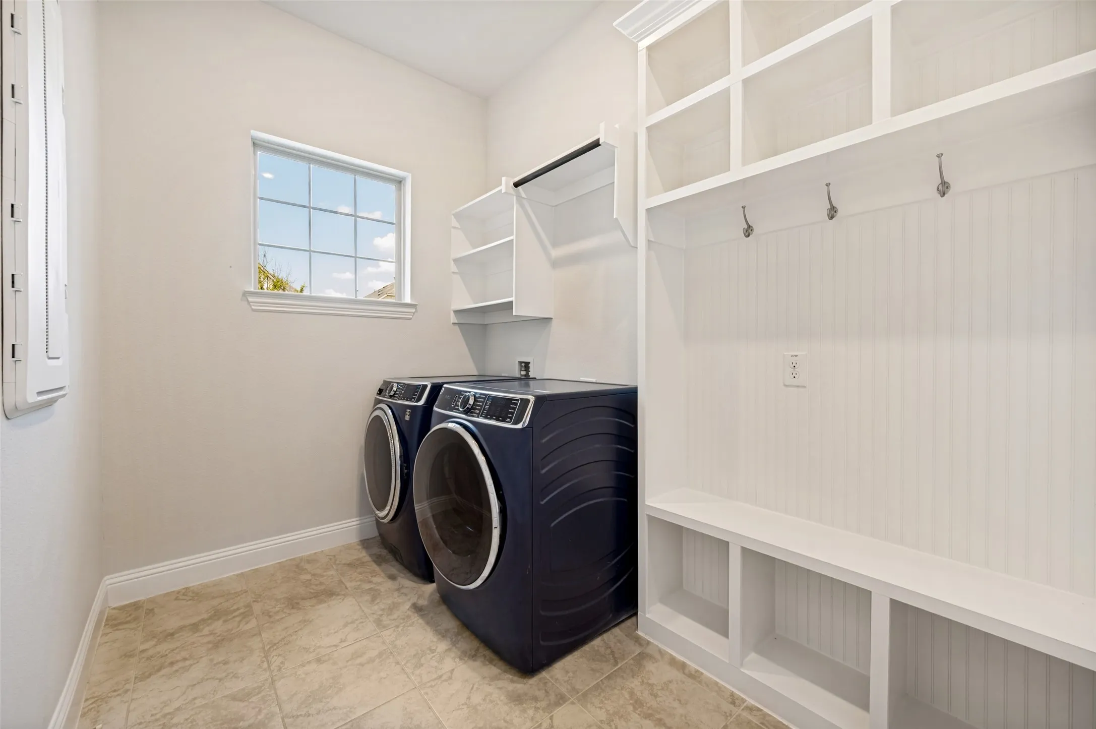 Spacious laundry room designed with both style and functionality in mind, featuring ample storage, built-in shelving, and a convenient mud area complete with bench seating, cubbies, and hooks. Natural light and generous floor space make everyday organization and laundry a breeze.