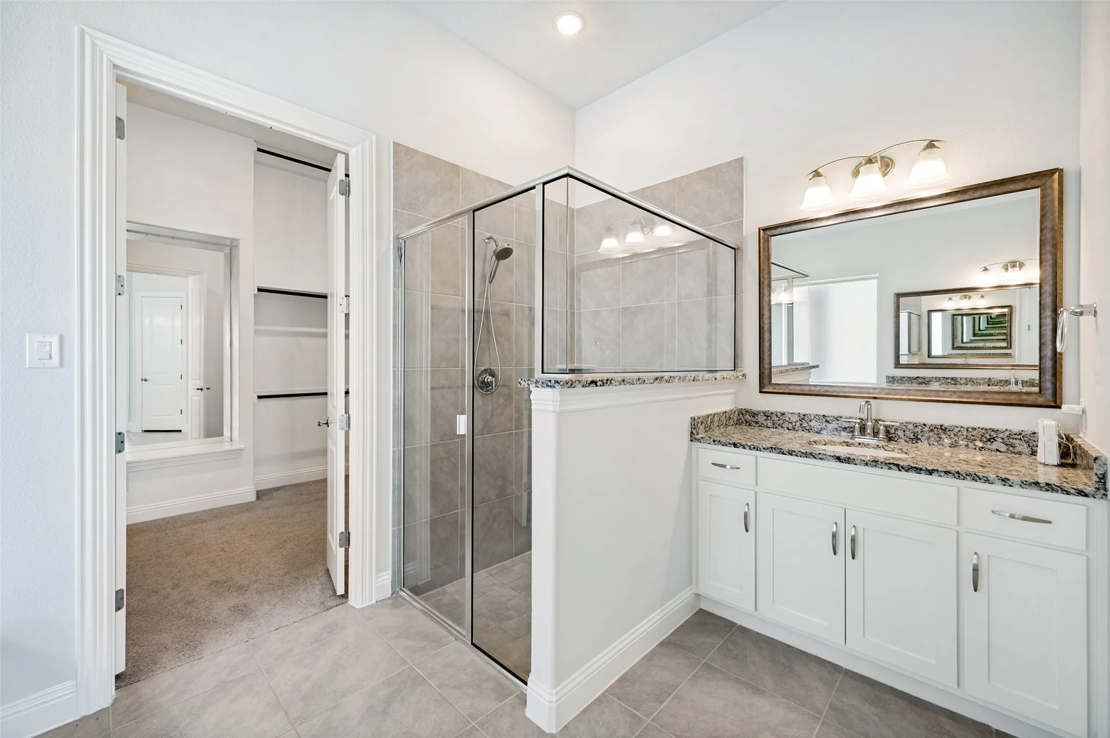 Spacious ensuite bath featuring a granite-topped vanity with abundant cabinetry, a large separate walk-in shower with glass enclosure, and neutral finishes throughout. The adjoining oversized walk-in closet provides exceptional storage and completes this comfortable, well-designed private suite.
