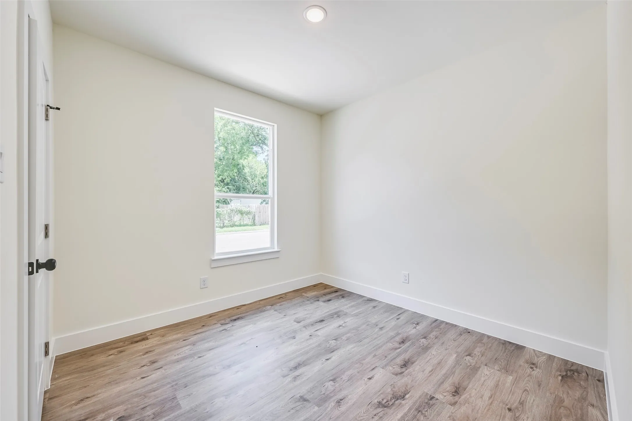 Room featuring wood-finish flooring, recessed ceiling light, white baseboards, and a window with a white frame