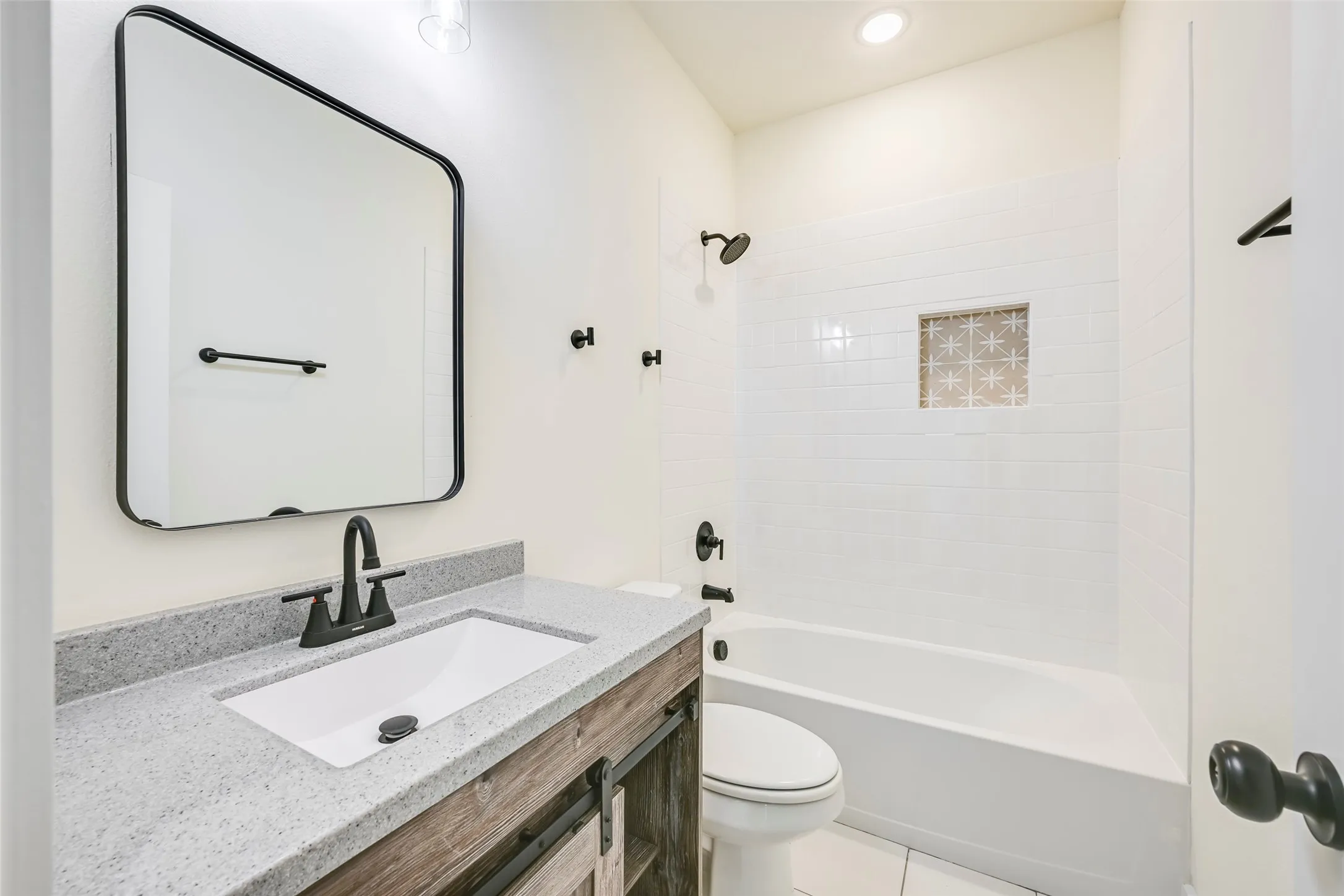 Bathroom featuring a white subway tile shower surround with a decorative niche, a white tub, and matte black fixtures