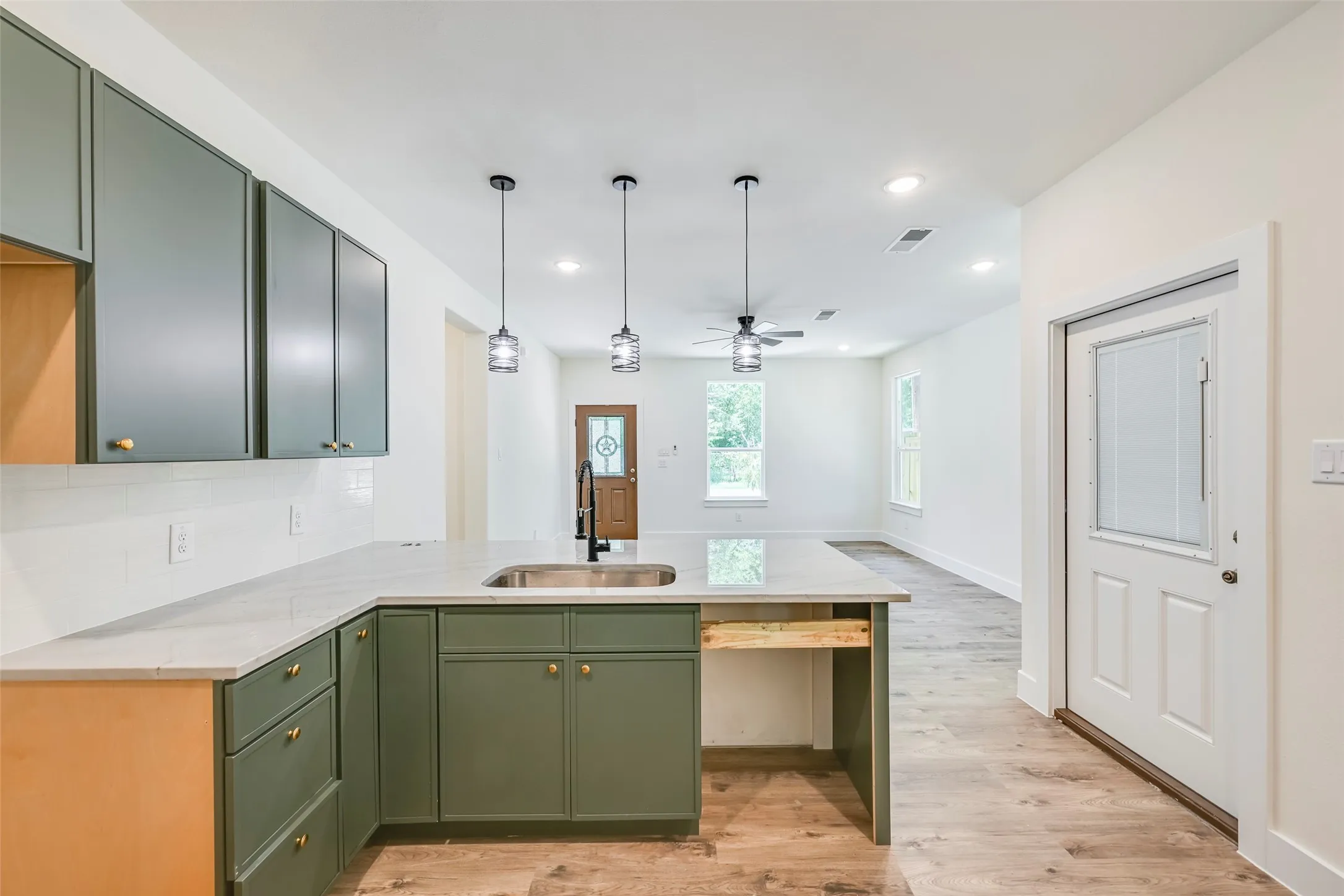 Kitchen island featuring an undermount sink, three pendant lights, and a light-toned countertop