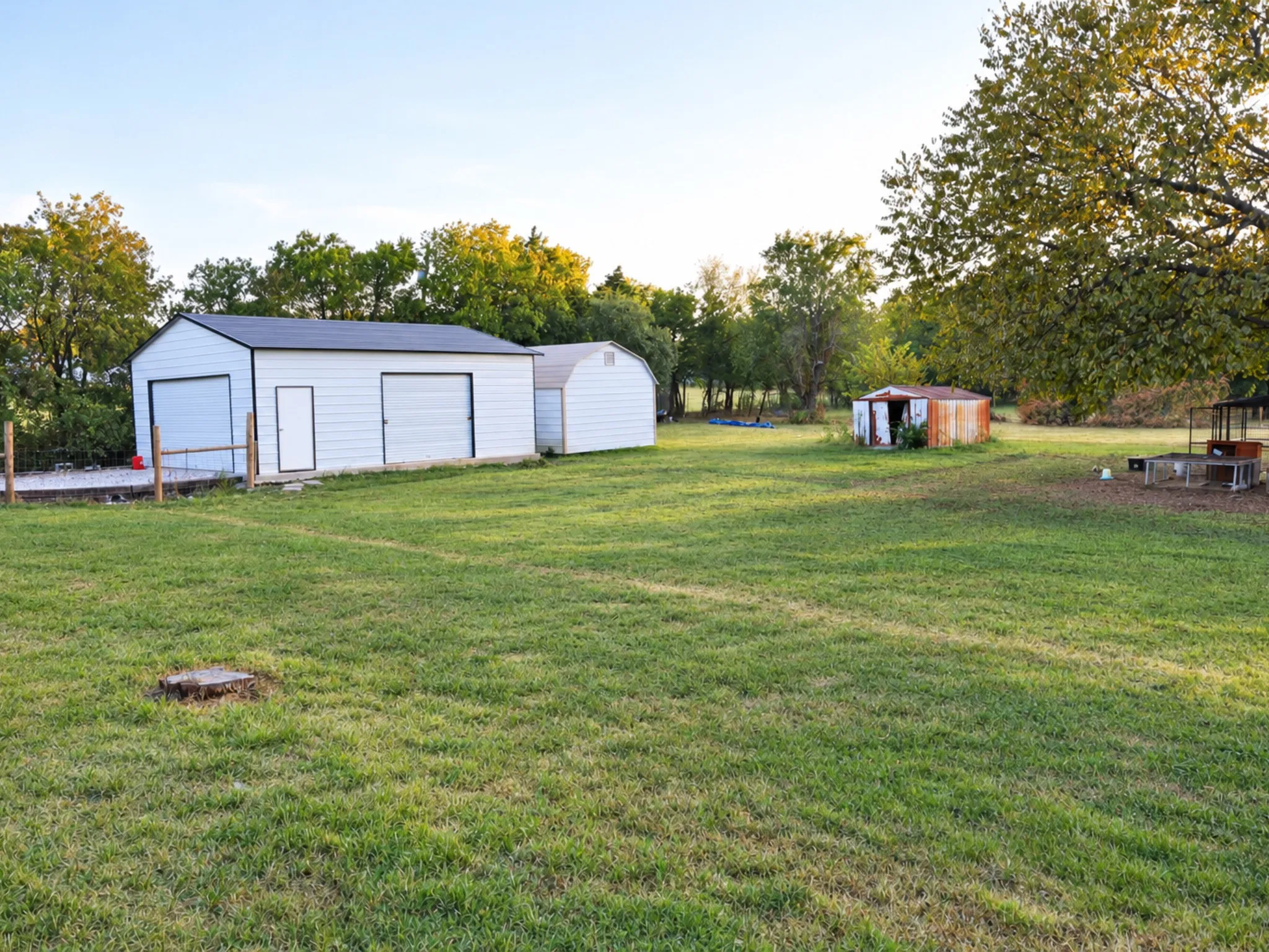 Expansive grassy area featuring a two-car garage with an additional service door, an attached utility shed, and a detached storage shed