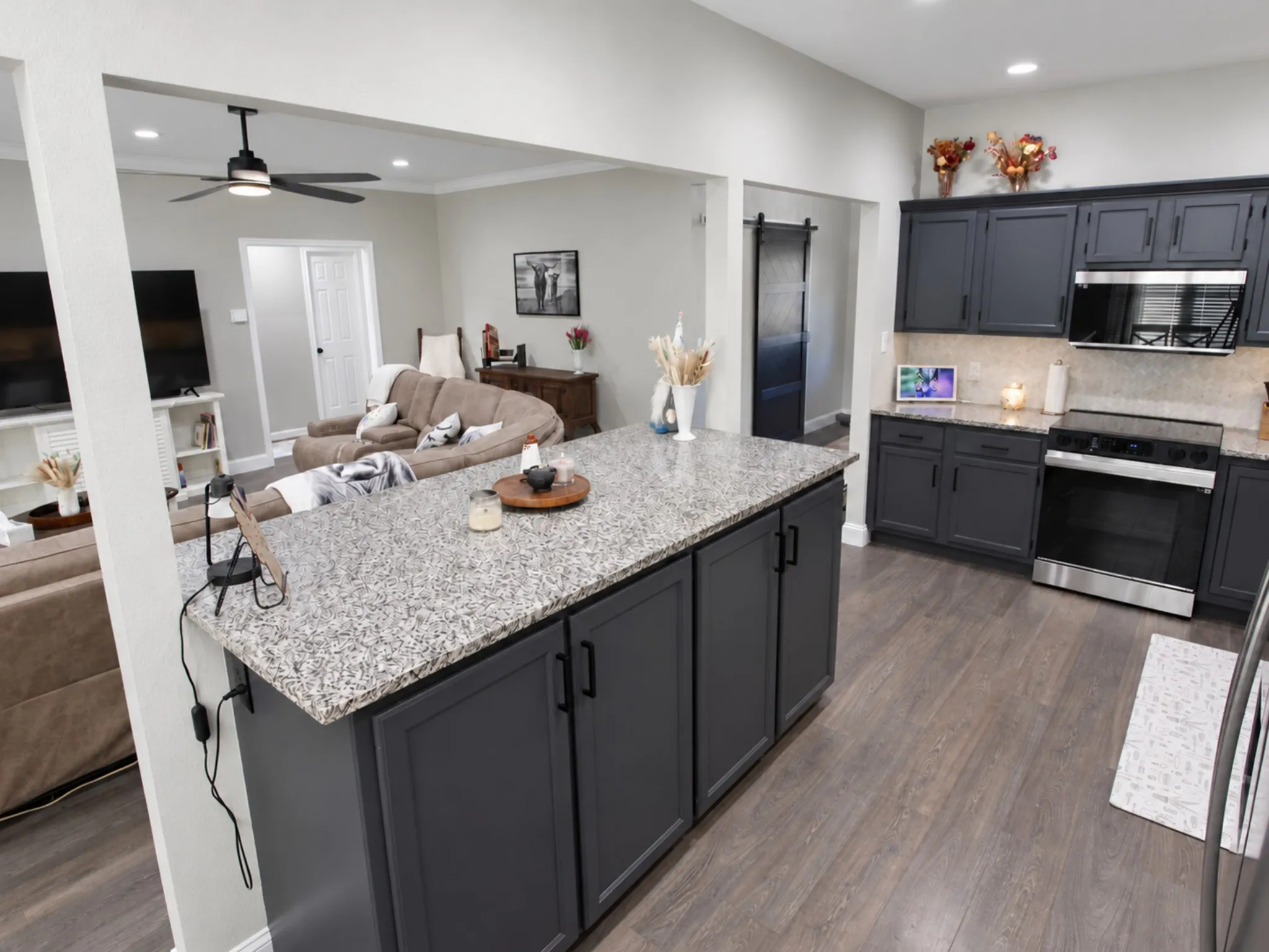 Kitchen island with stone-finish countertop, dark shaker-style cabinetry, stainless steel appliances, and wood-finish flooring