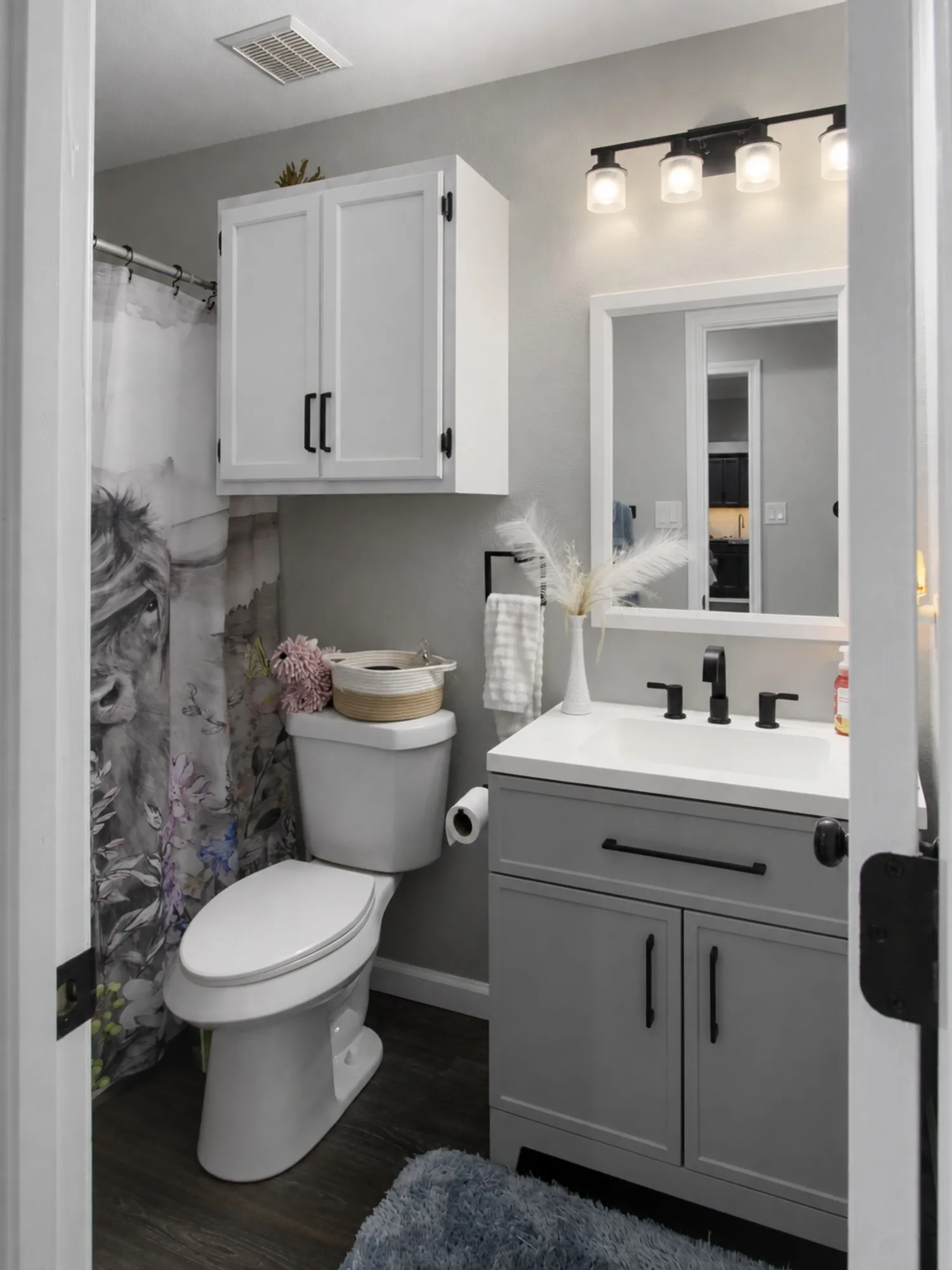 Bathroom featuring wood-finish flooring, a white vanity with an integrated sink, matte black fixtures, a white wall-mounted cabinet, and a framed mirror