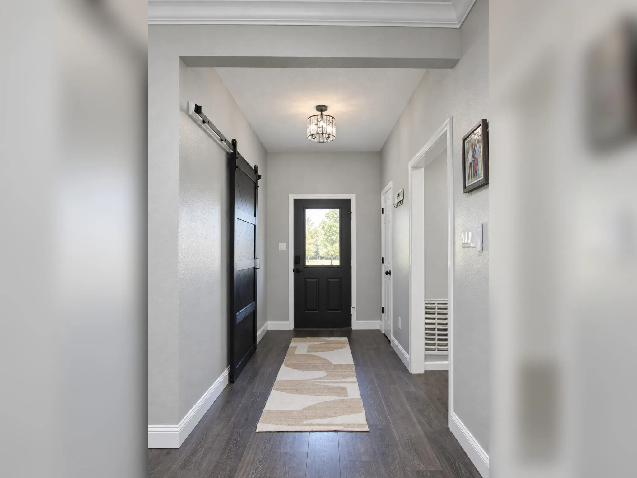 Wood-finish flooring, crown molding, barn door, decorative flush mount lighting, and a front entry door with glass paneling