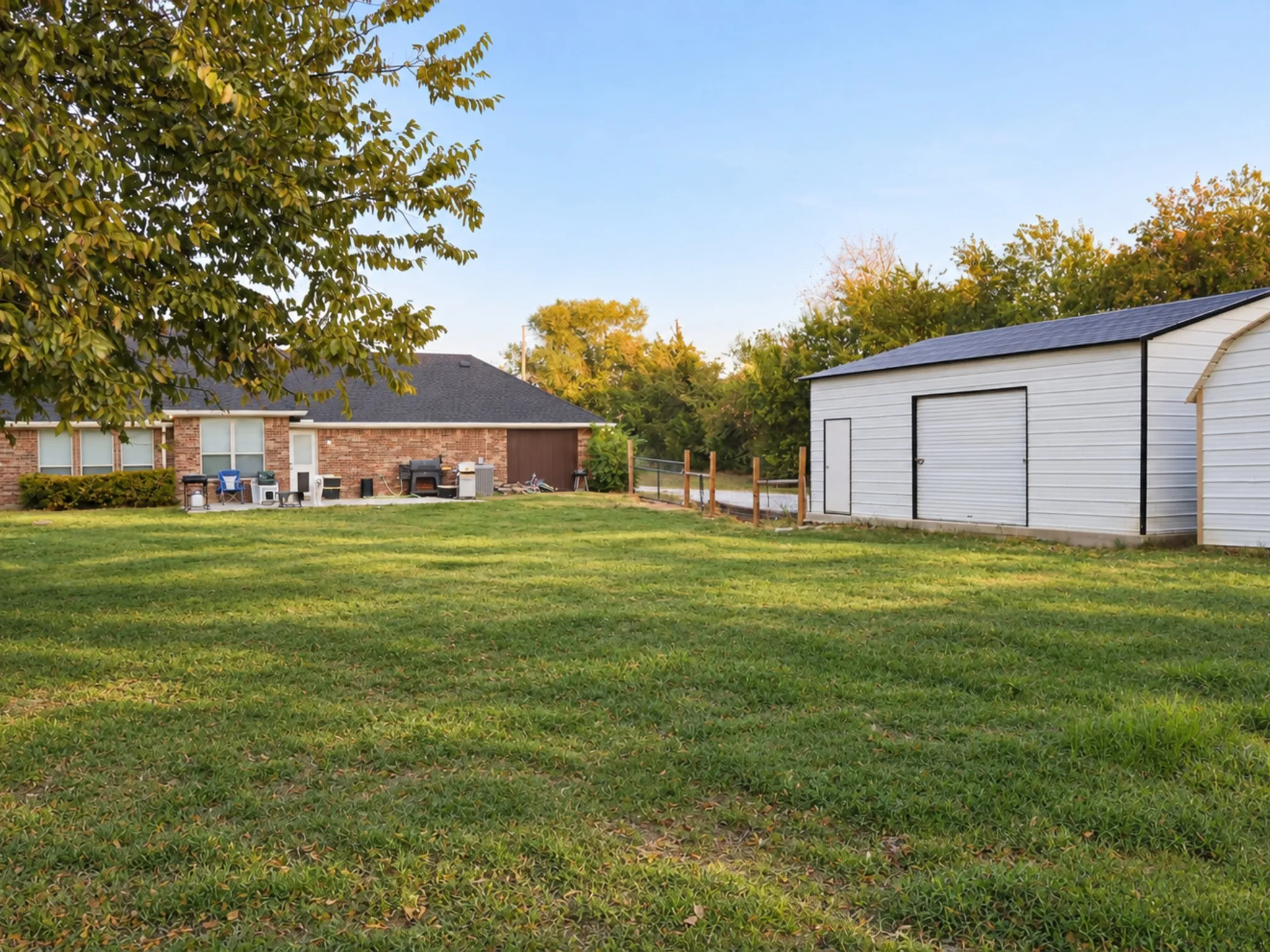 Expansive green lawn with a white metal outbuilding featuring a garage door and side entry