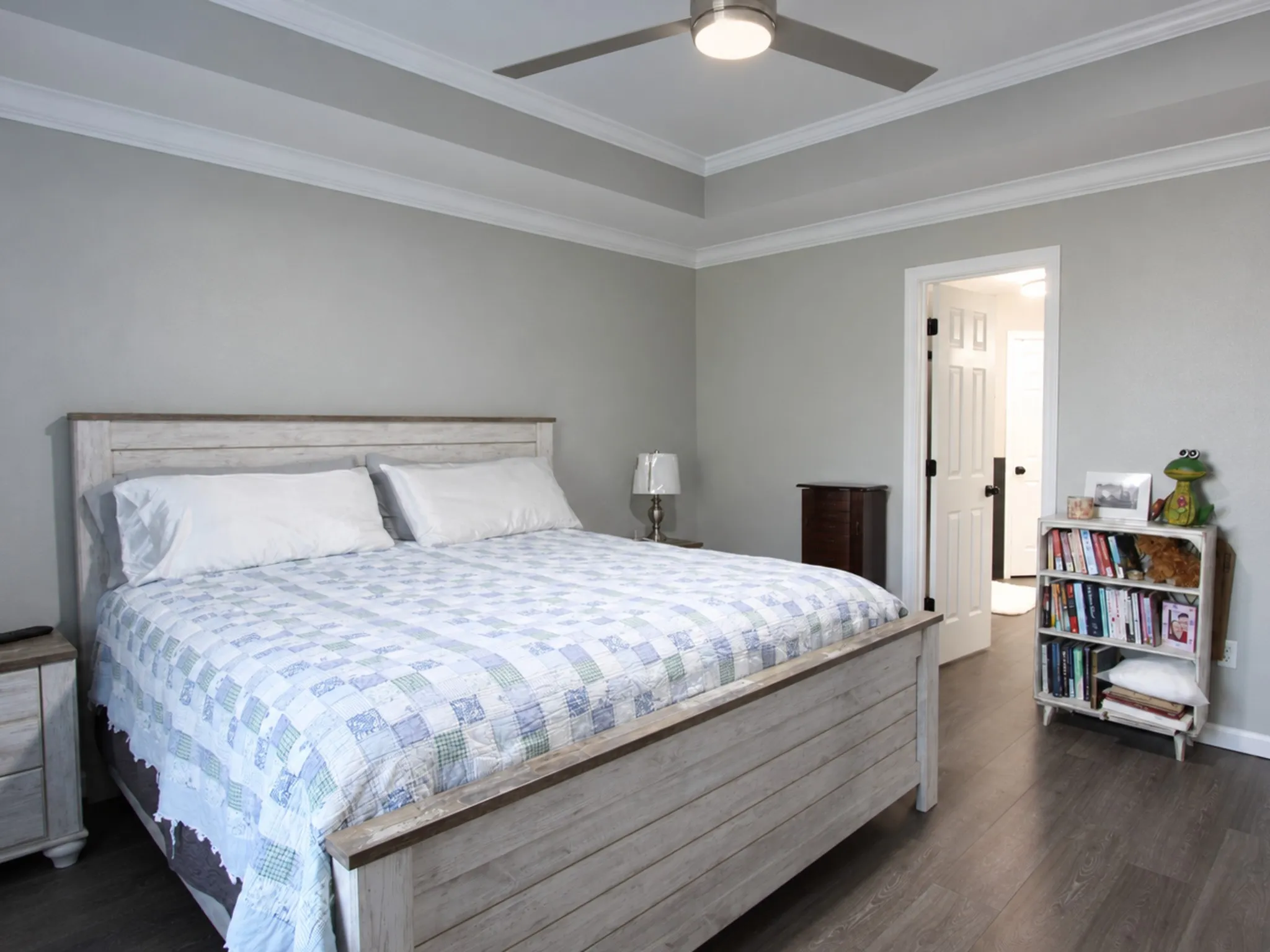 Tray ceiling with crown molding, wood-finish flooring, and a ceiling fan with integrated lighting