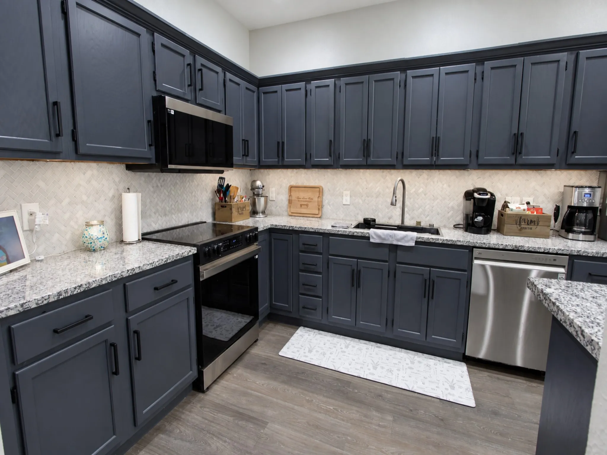 Galley kitchen featuring dark cabinetry, speckled countertops, stainless steel appliances, a white tile backsplash, and wood-finish flooring