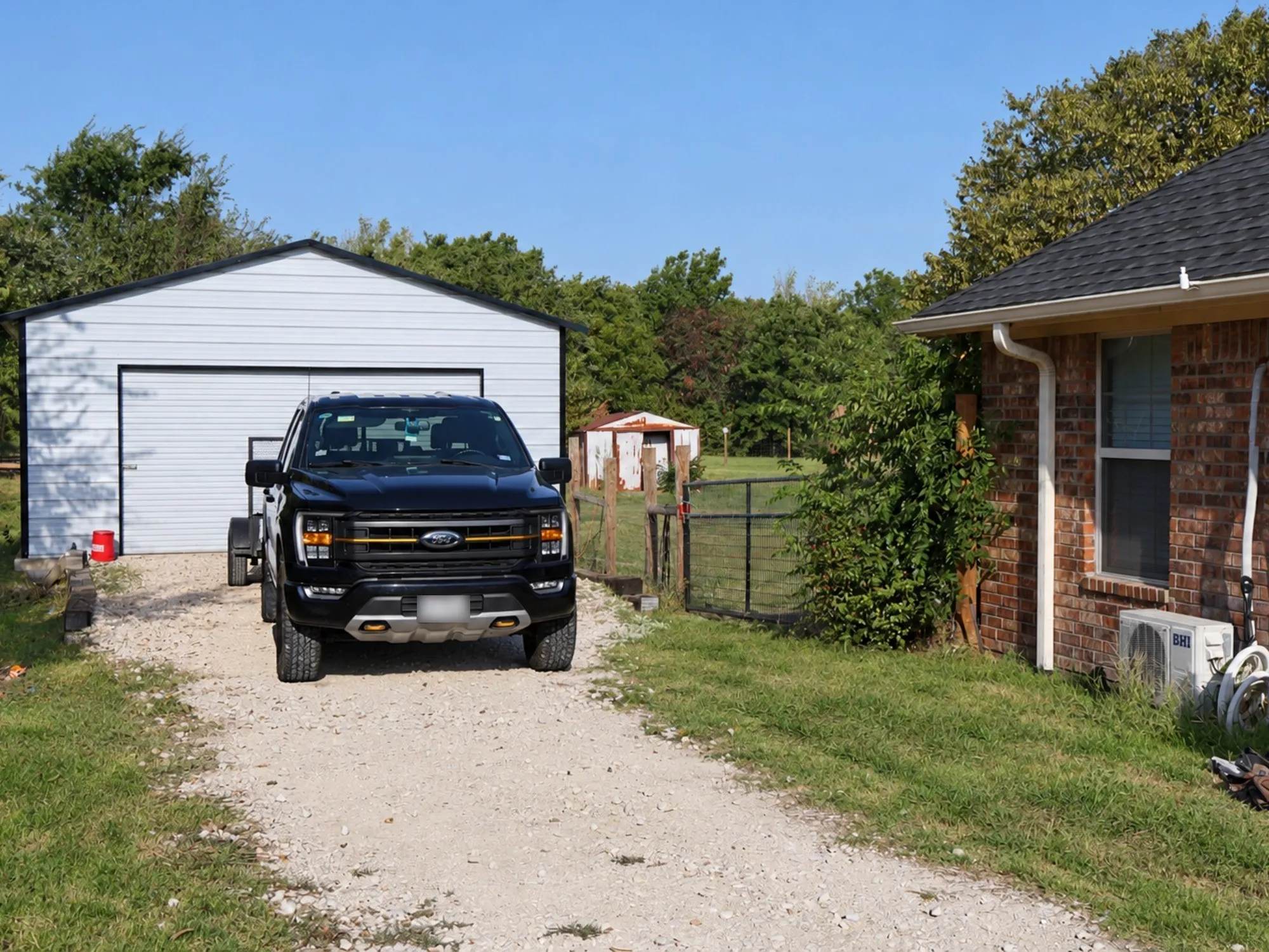 Gravel driveway, brick exterior, dedicated garage, fenced enclosure, and mature trees
