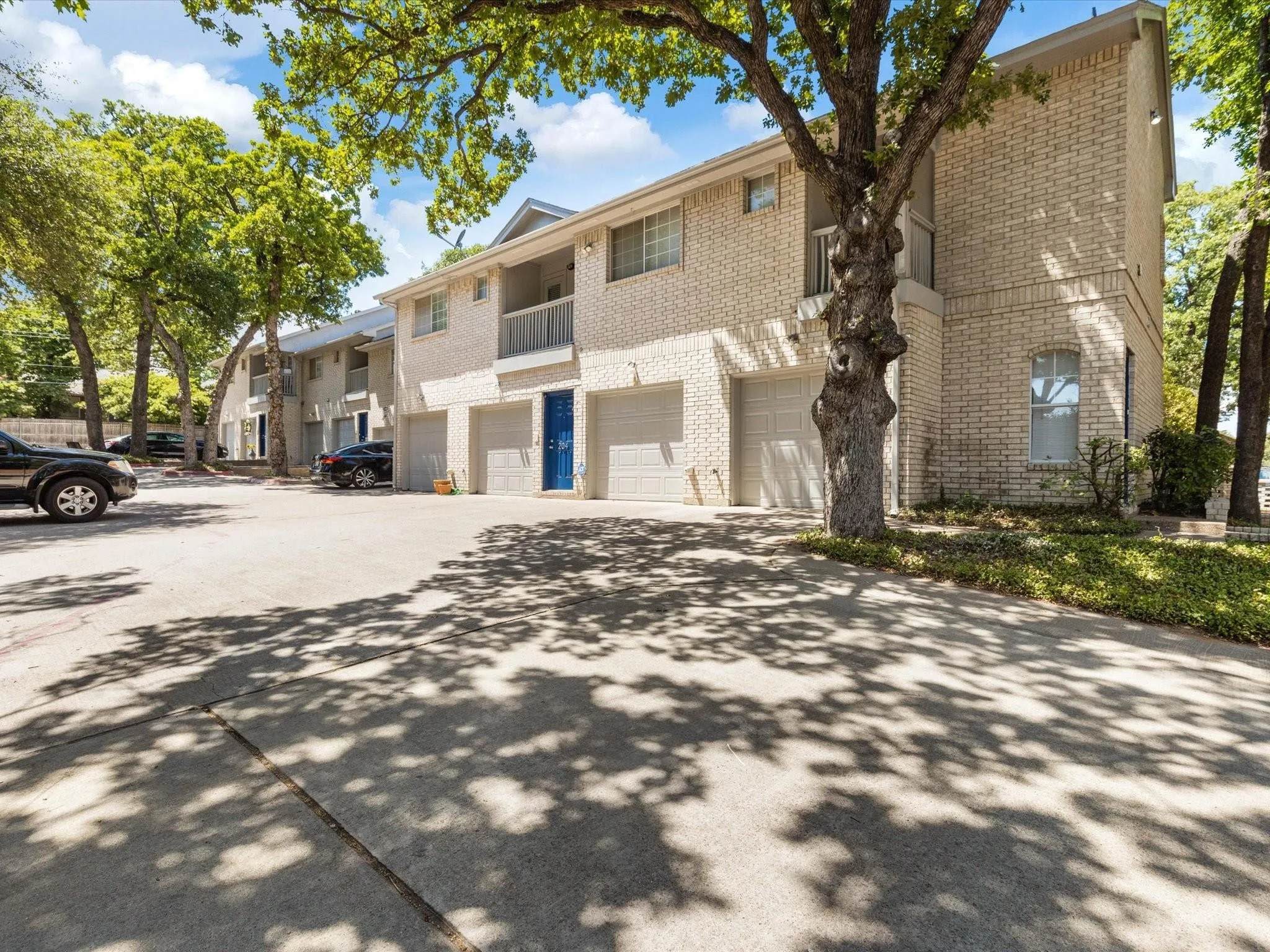 Brick exterior with individual garages, mature trees, and concrete paving