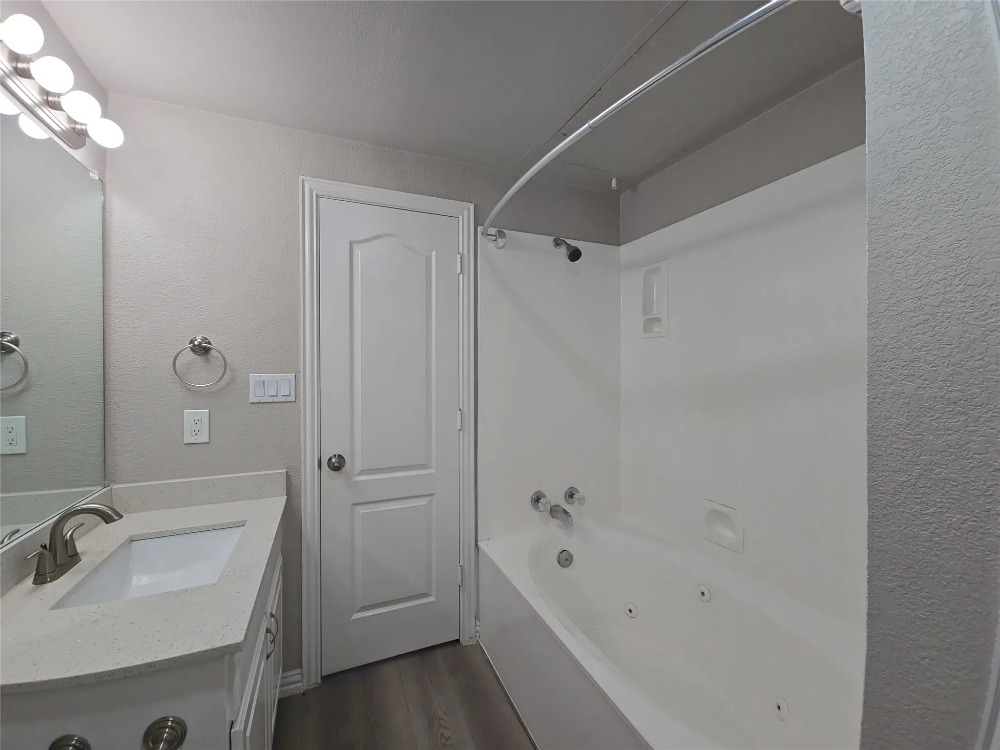 Jetted bathtub with shower, vanity with integrated sink, stone-finish countertop, and wood-finish flooring
