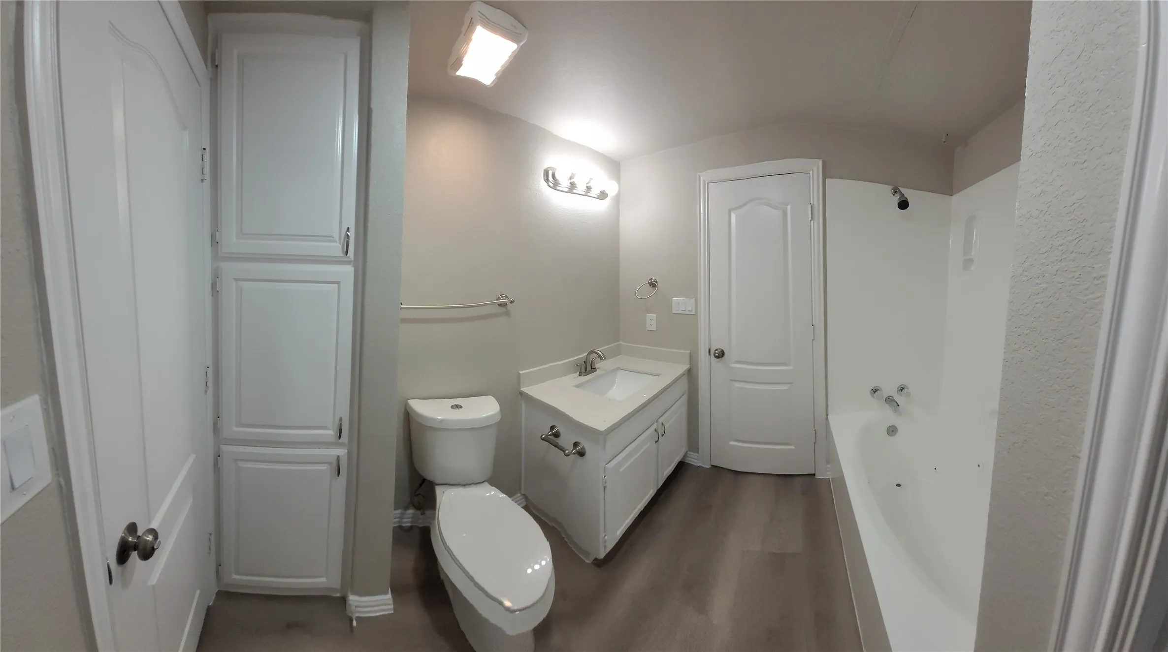 White cabinetry with integrated storage, single vanity with countertop, light wood-finish flooring, toilet, and bathtub with shower