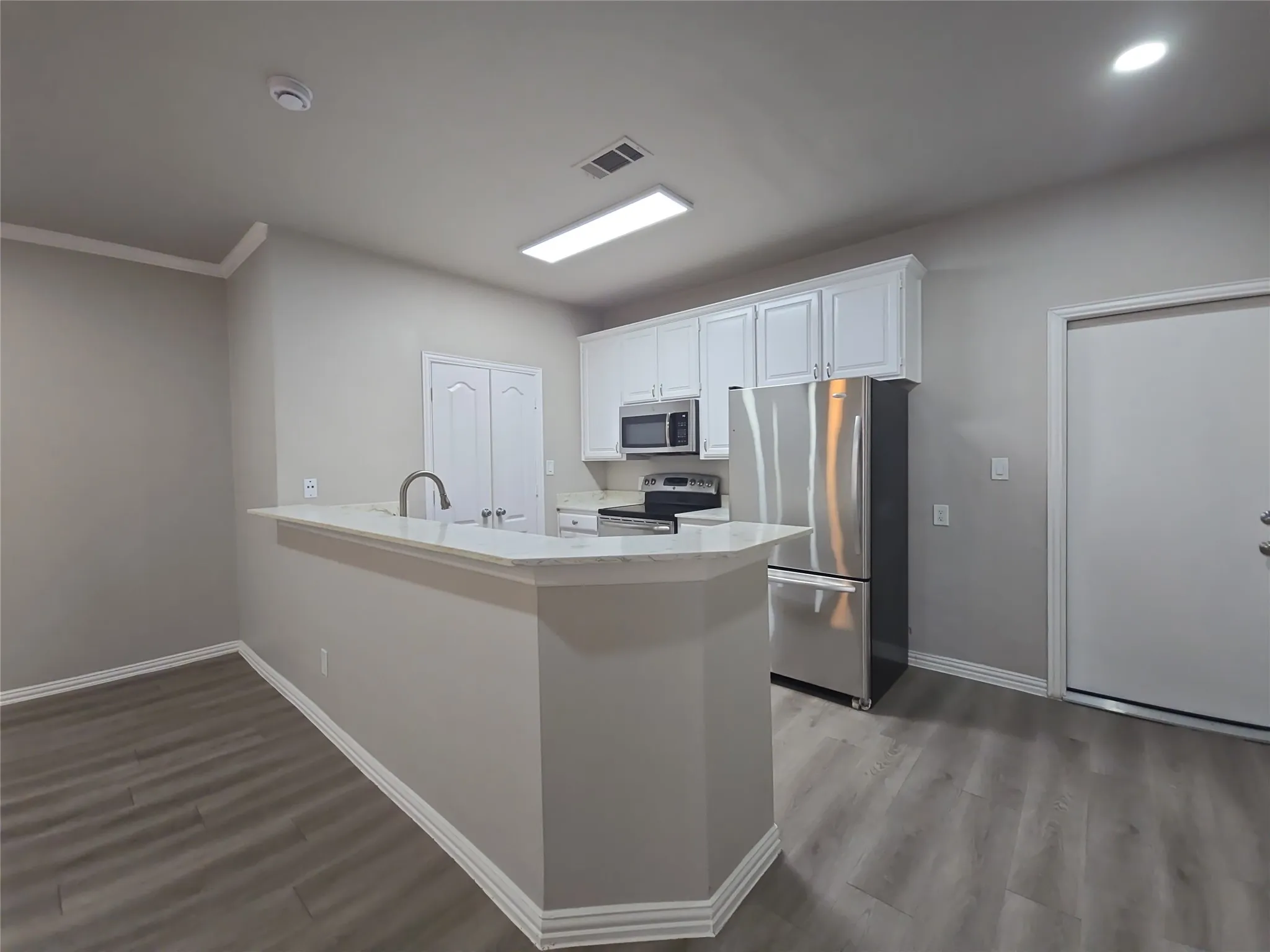 Kitchen featuring white cabinetry, stainless steel appliances, a breakfast bar with a solid surface countertop, and wood-finish flooring